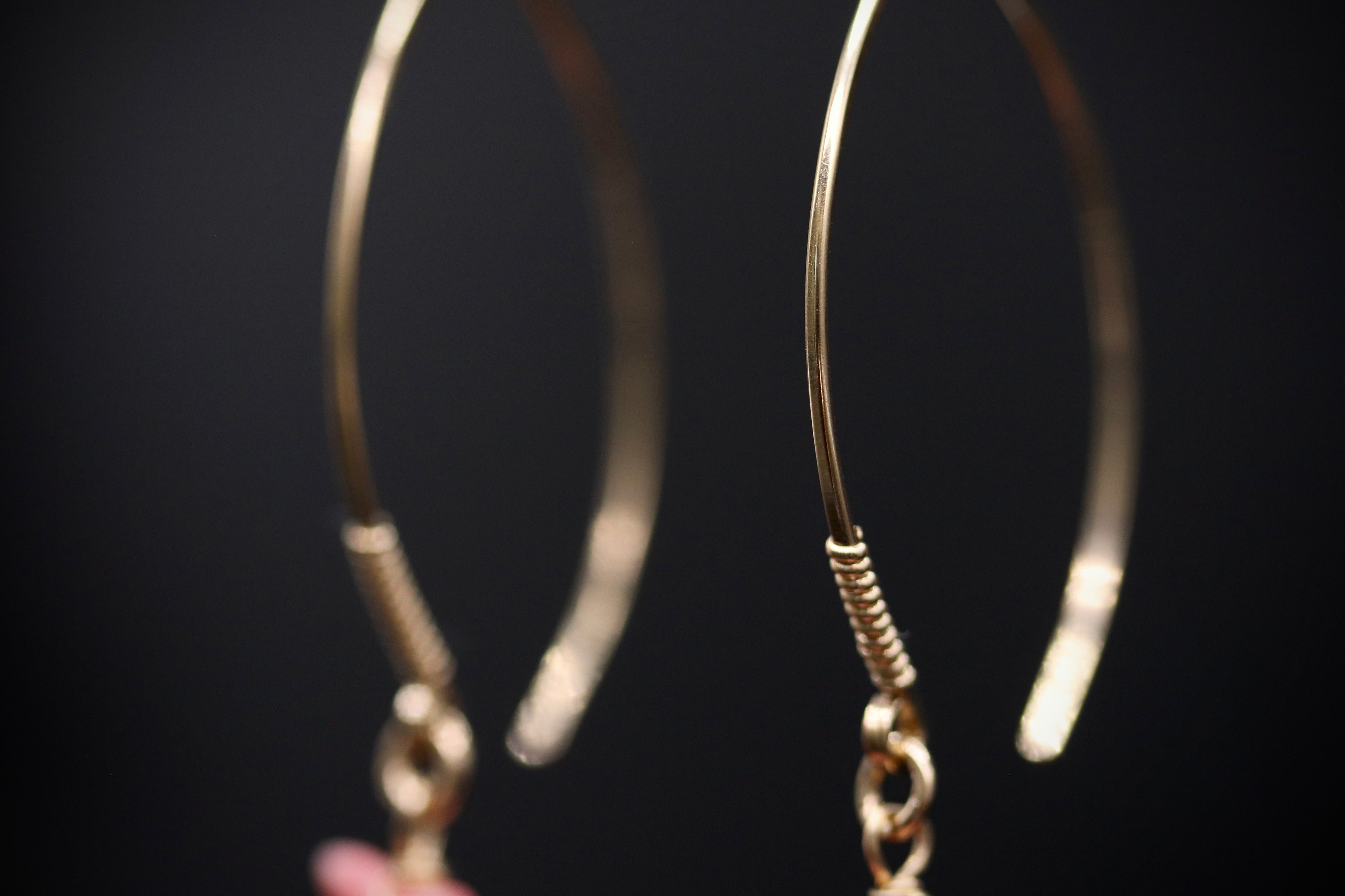 A close-up view of a pair of gold hoop earrings with a dark background.