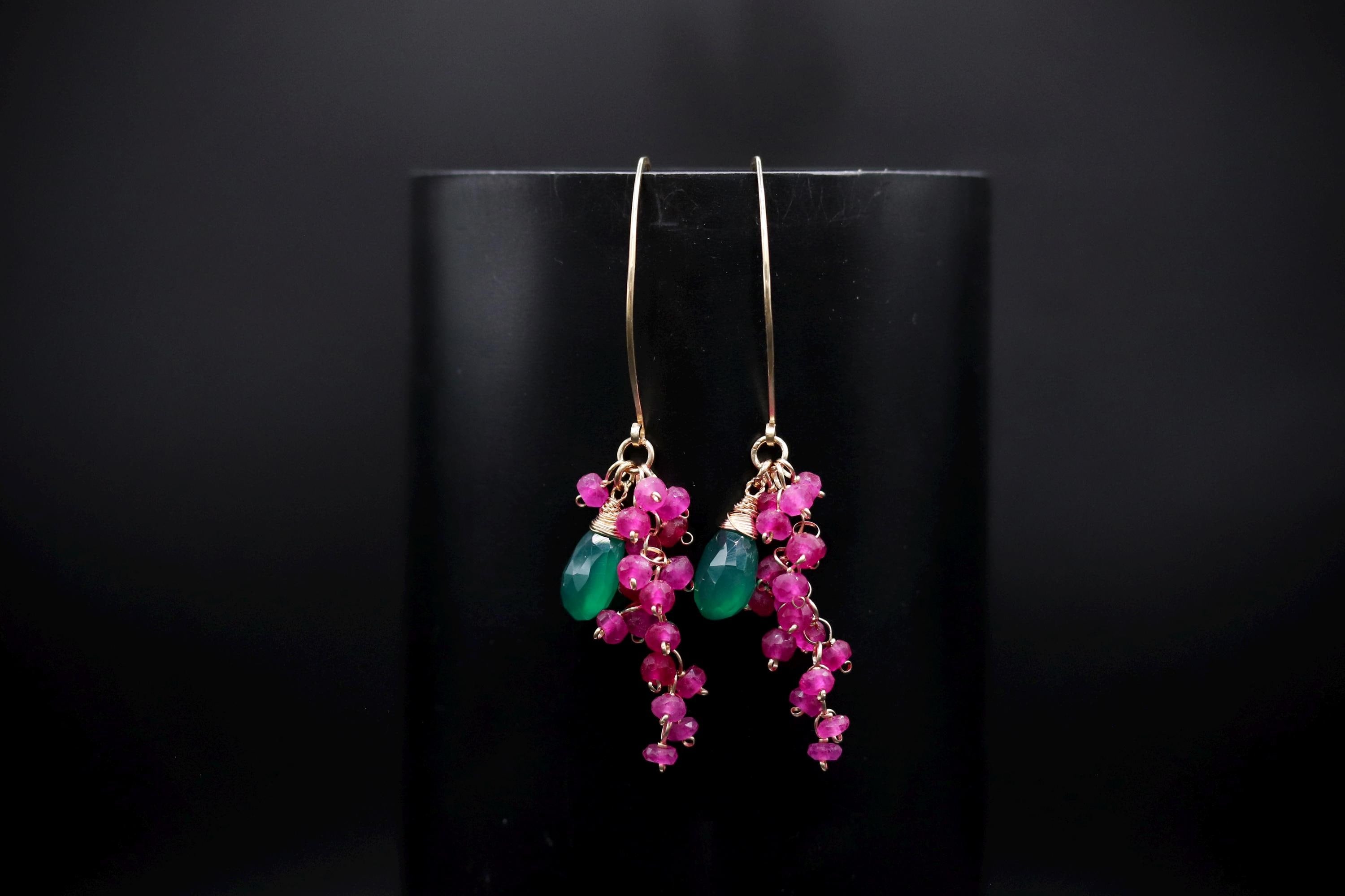 A pair of earrings with a black background and a pair of dangling earrings with green and pink gemstones.