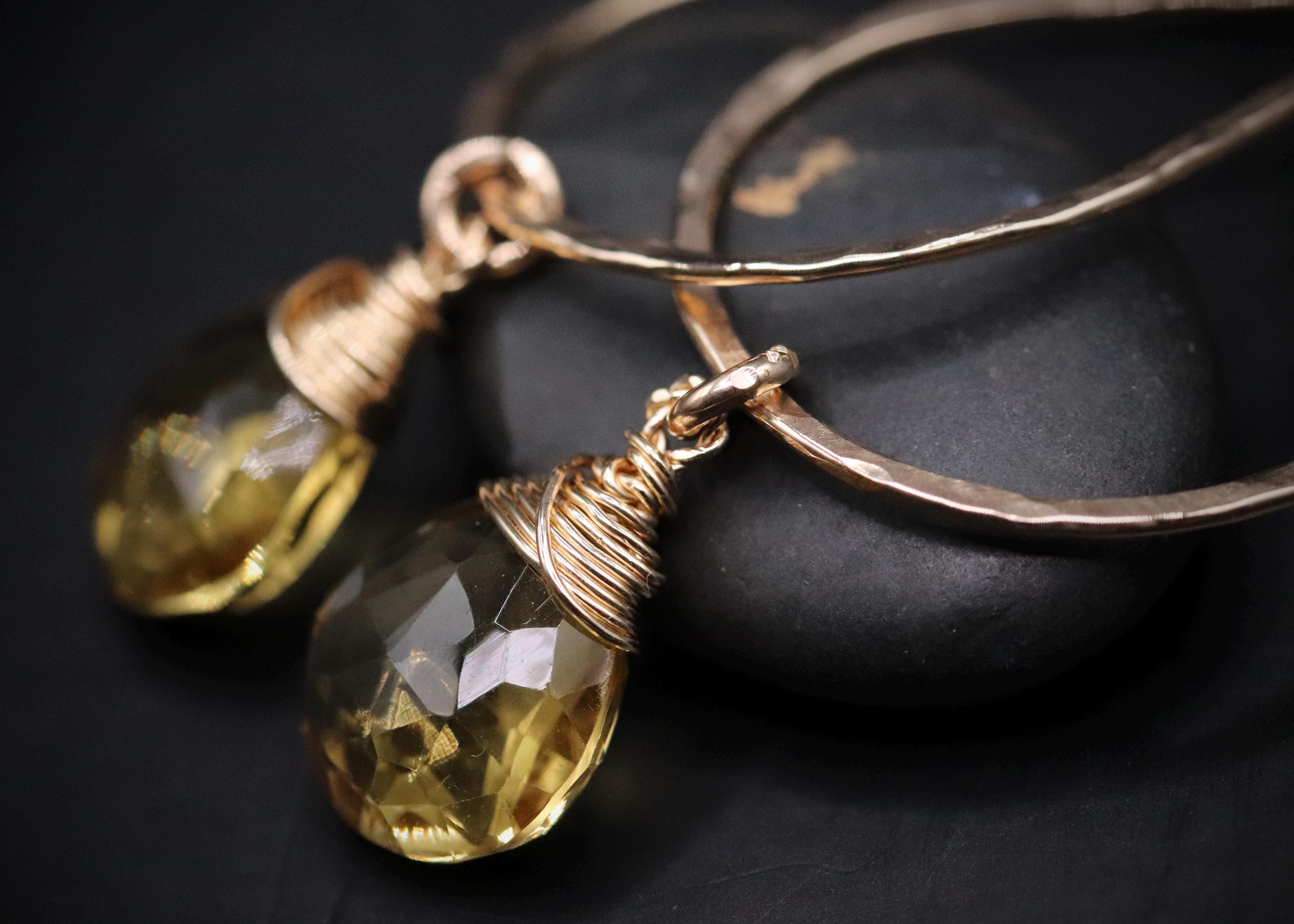 A pair of gold hoop earrings with clear gemstone pendants resting on a black surface.