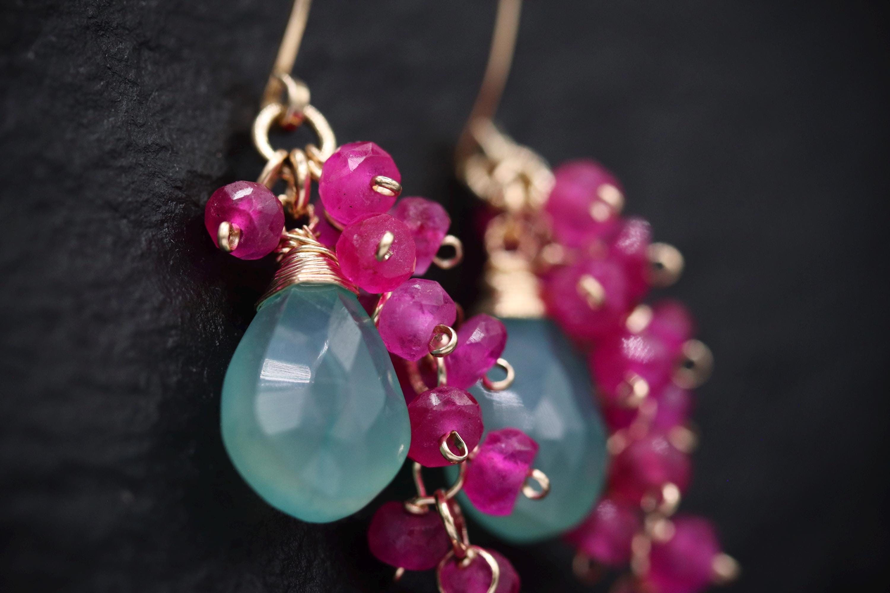A close-up view of a pair of earrings with a combination of blue and pink gemstones, as well as small, dangling charms.