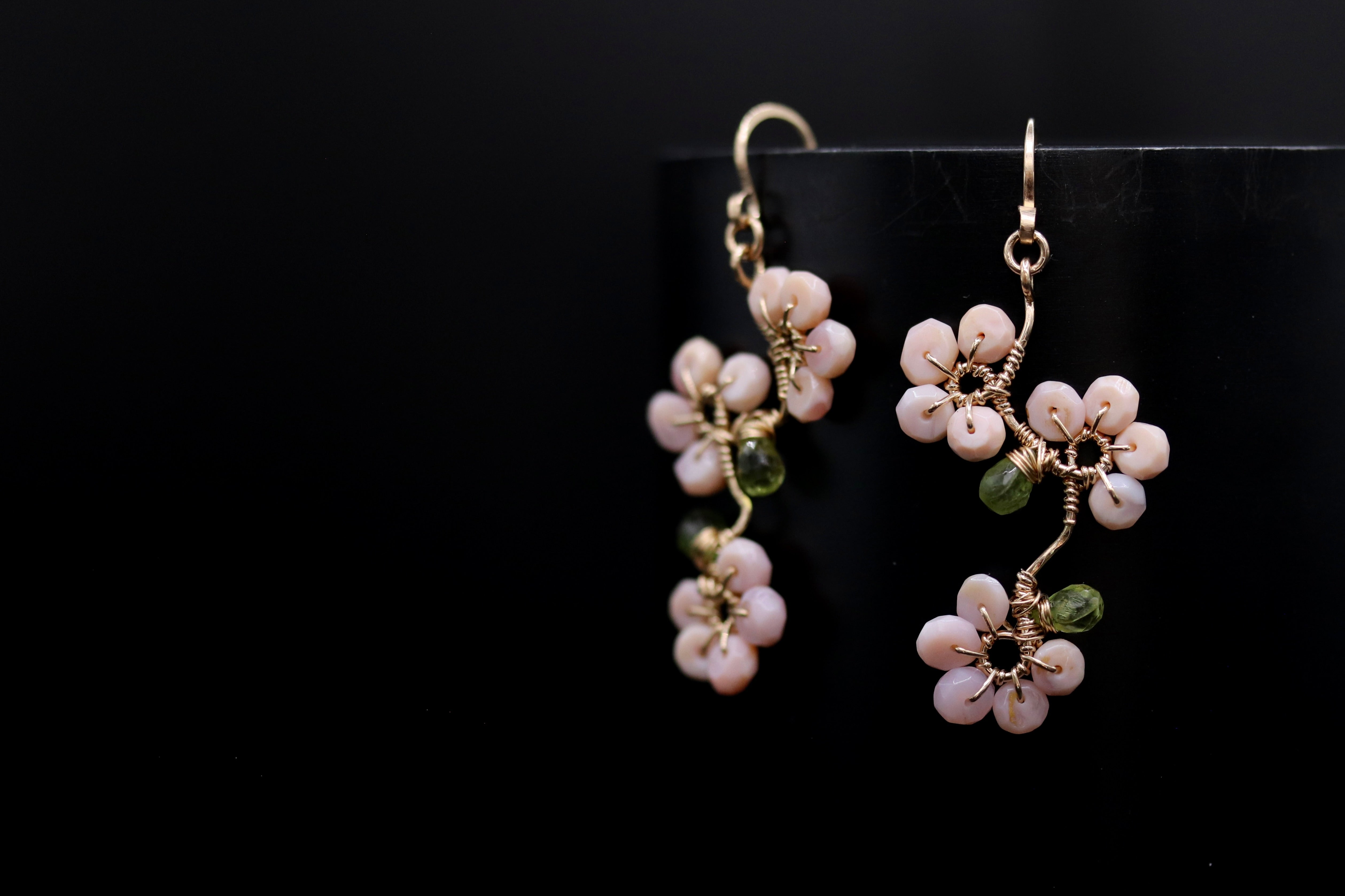 A pair of delicate earrings with white and green beads, hanging against a black background.