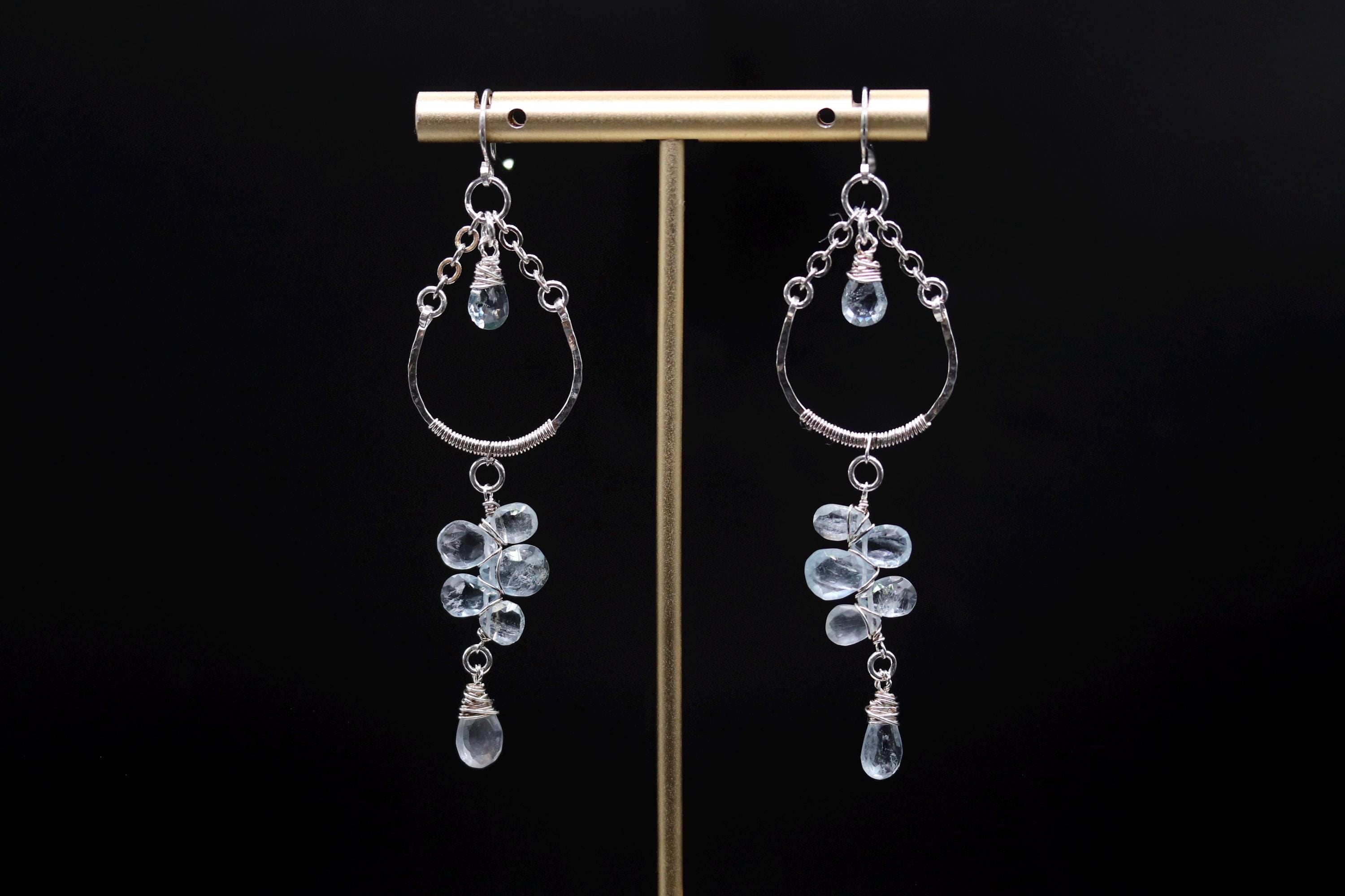 A pair of elegant earrings with dangling crystal stones, displayed on a gold stand against a black background.