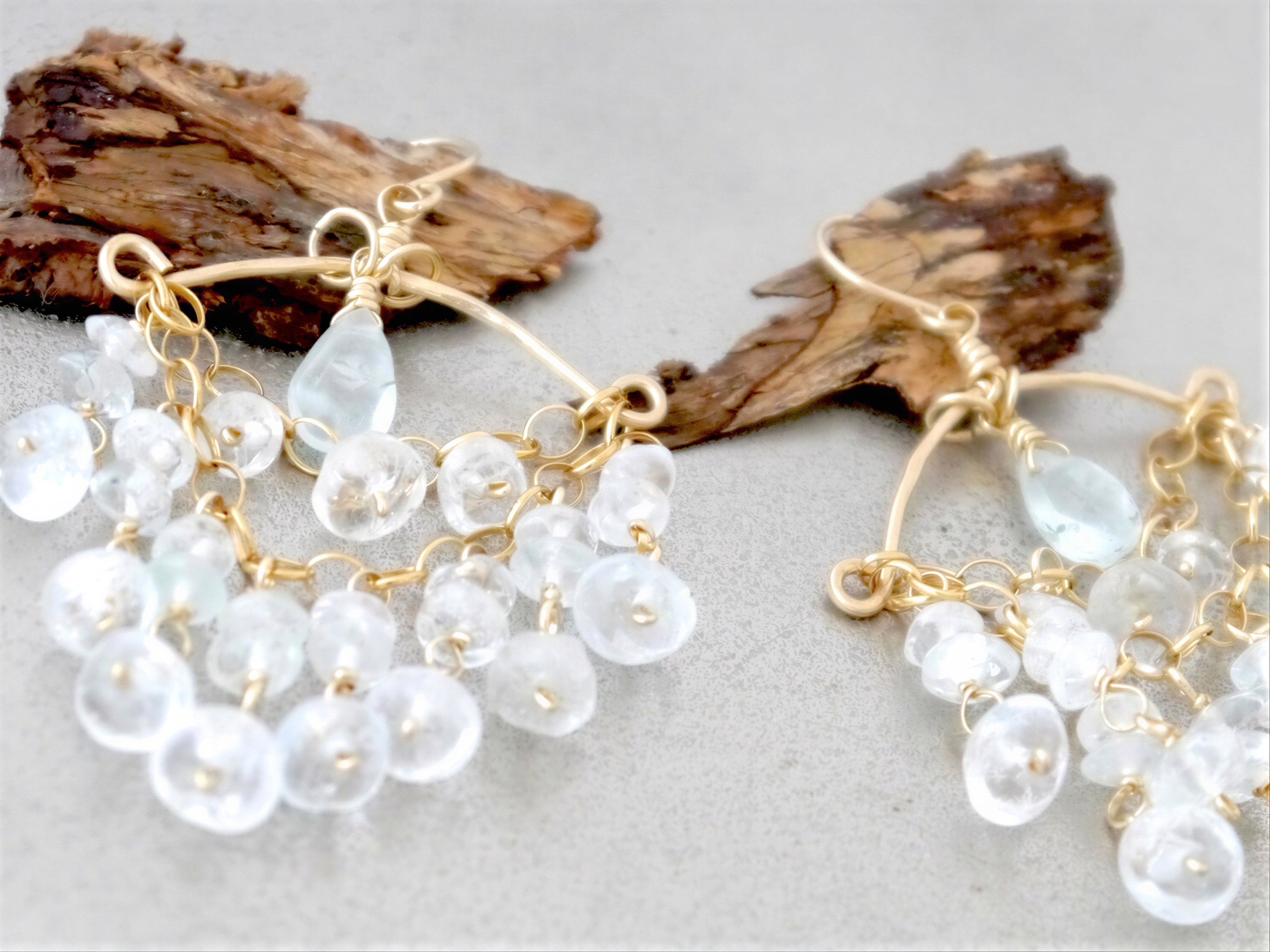 A pair of elegant earrings with clear beads and gold metal, resting on a wooden surface.