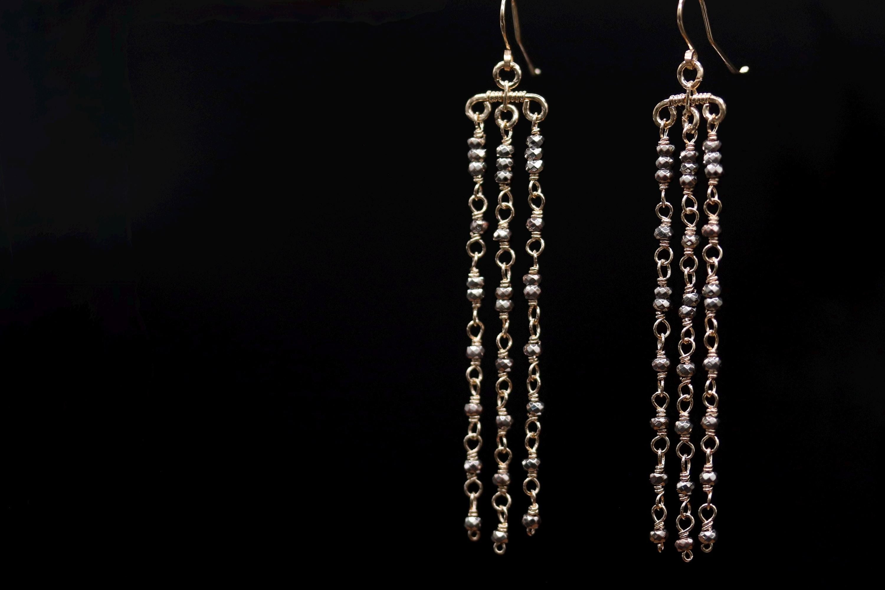 A pair of elegant earrings with long, dangling chains against a black background.
