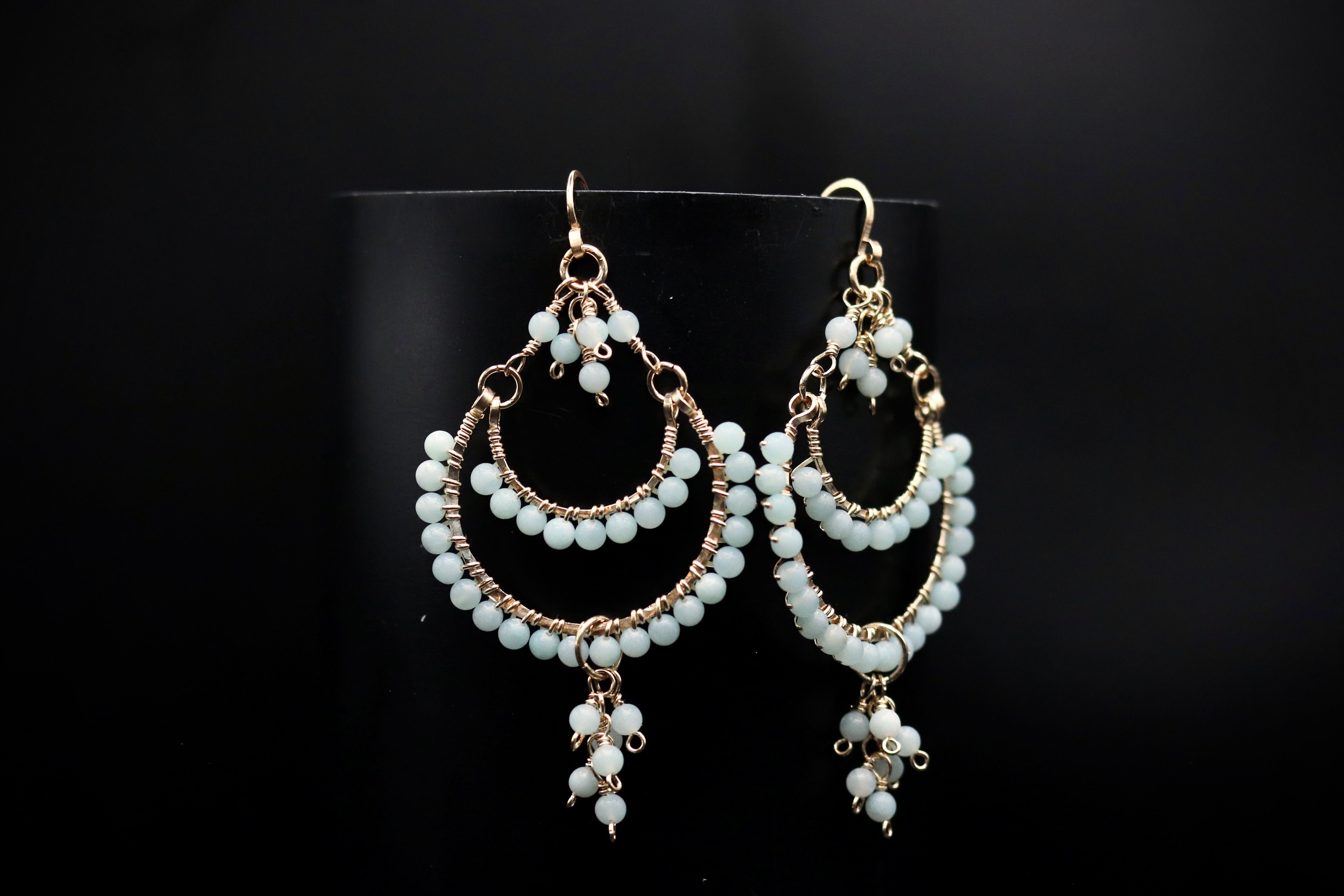 A pair of elegant white earrings with multiple tiers of dangling beads, displayed against a black background.