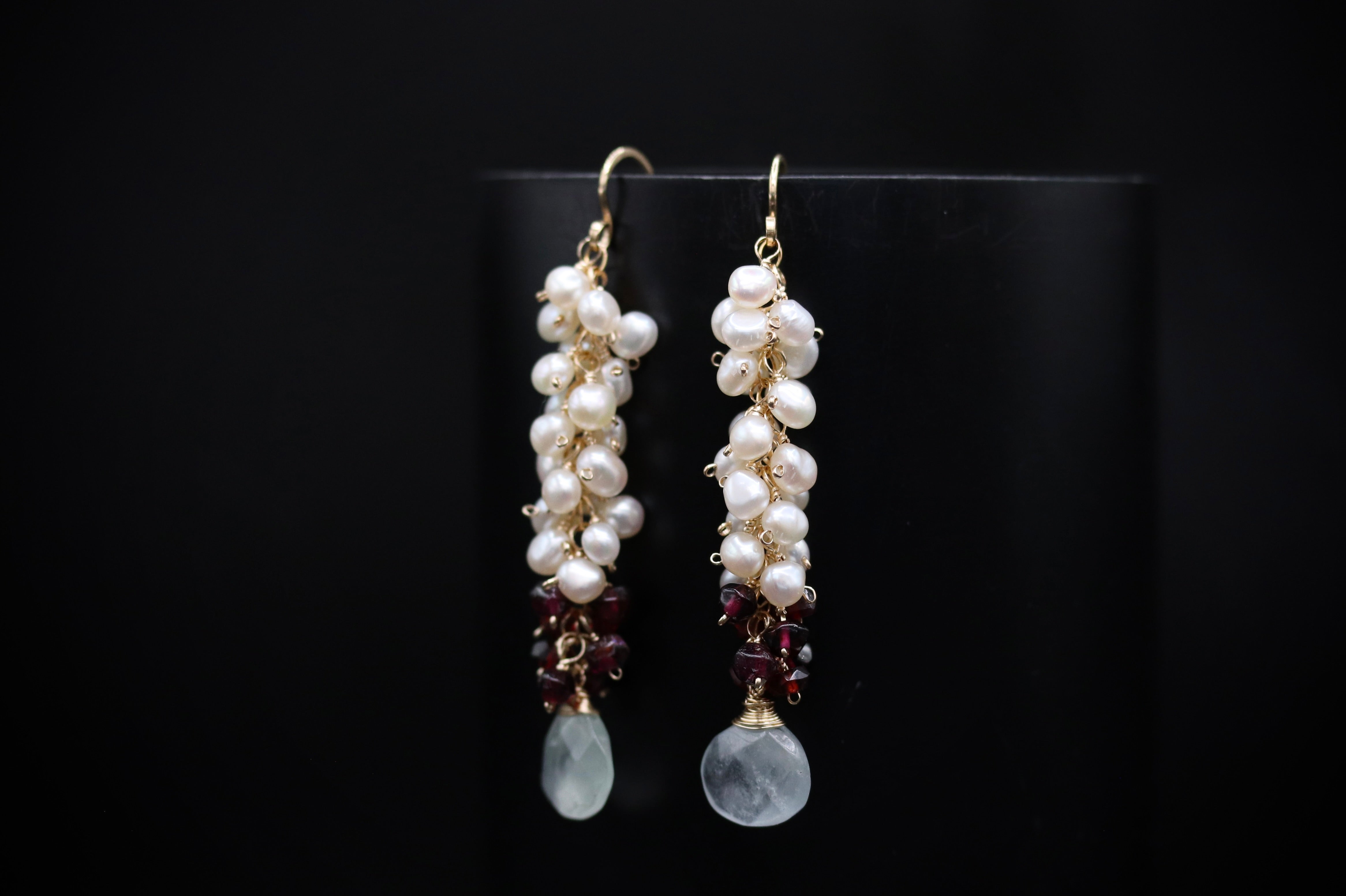 A pair of elegant earrings with white pearls and maroon gemstones hanging from the ends.
