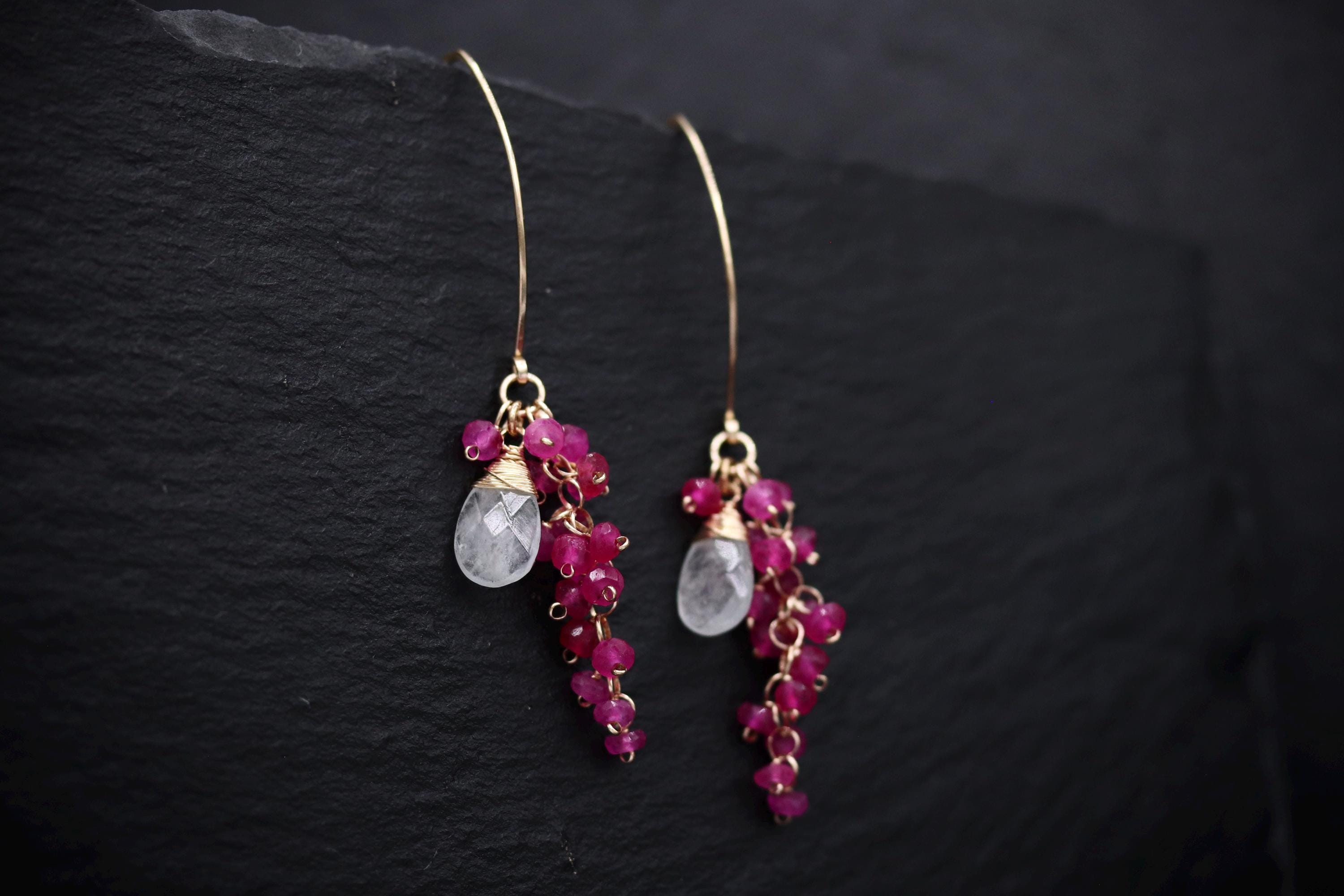 A pair of elegant earrings with a clear gemstone and a cluster of red gemstones hanging from the earrings.