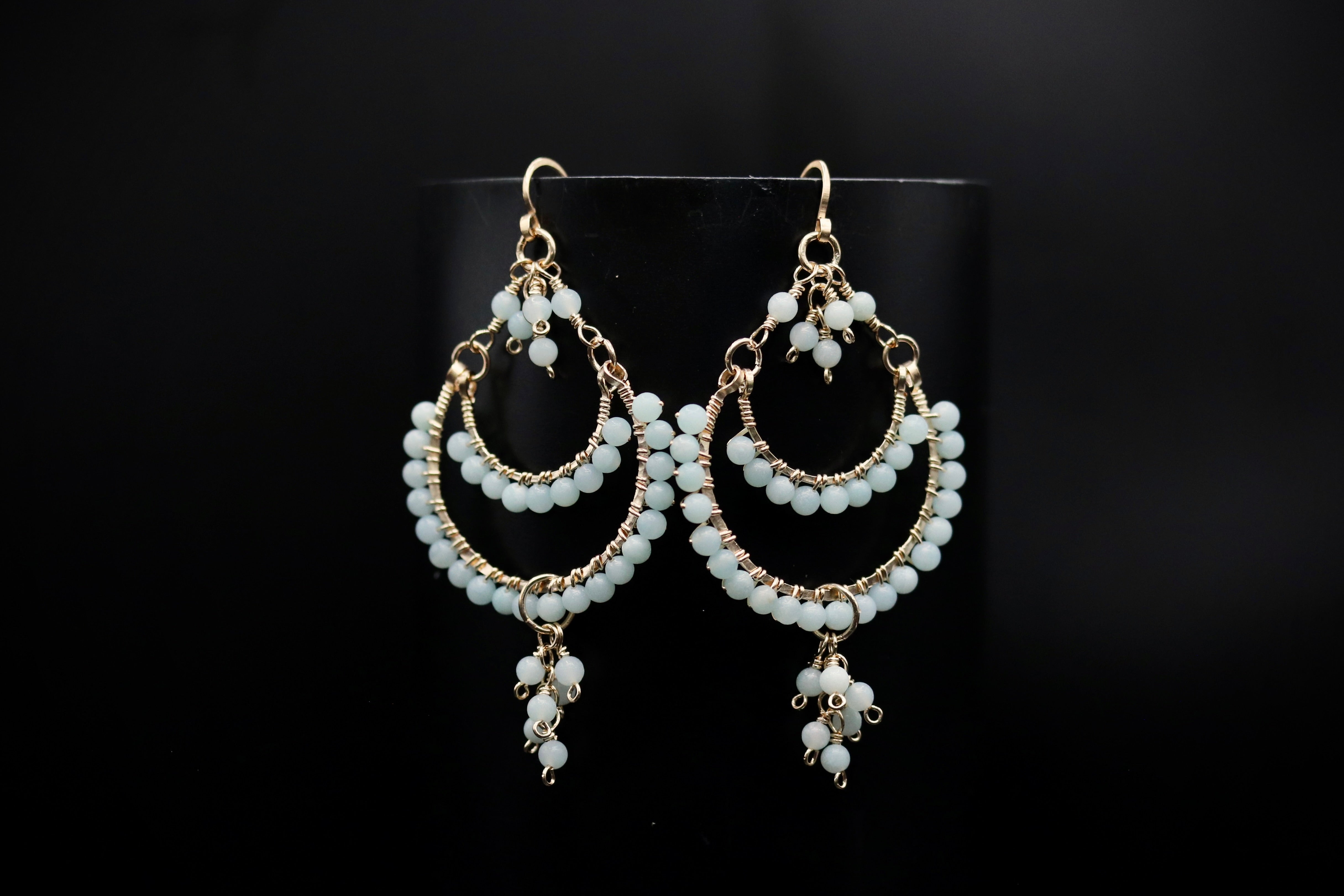 A pair of elegant earrings with white beads and dangling charms, displayed against a black background.