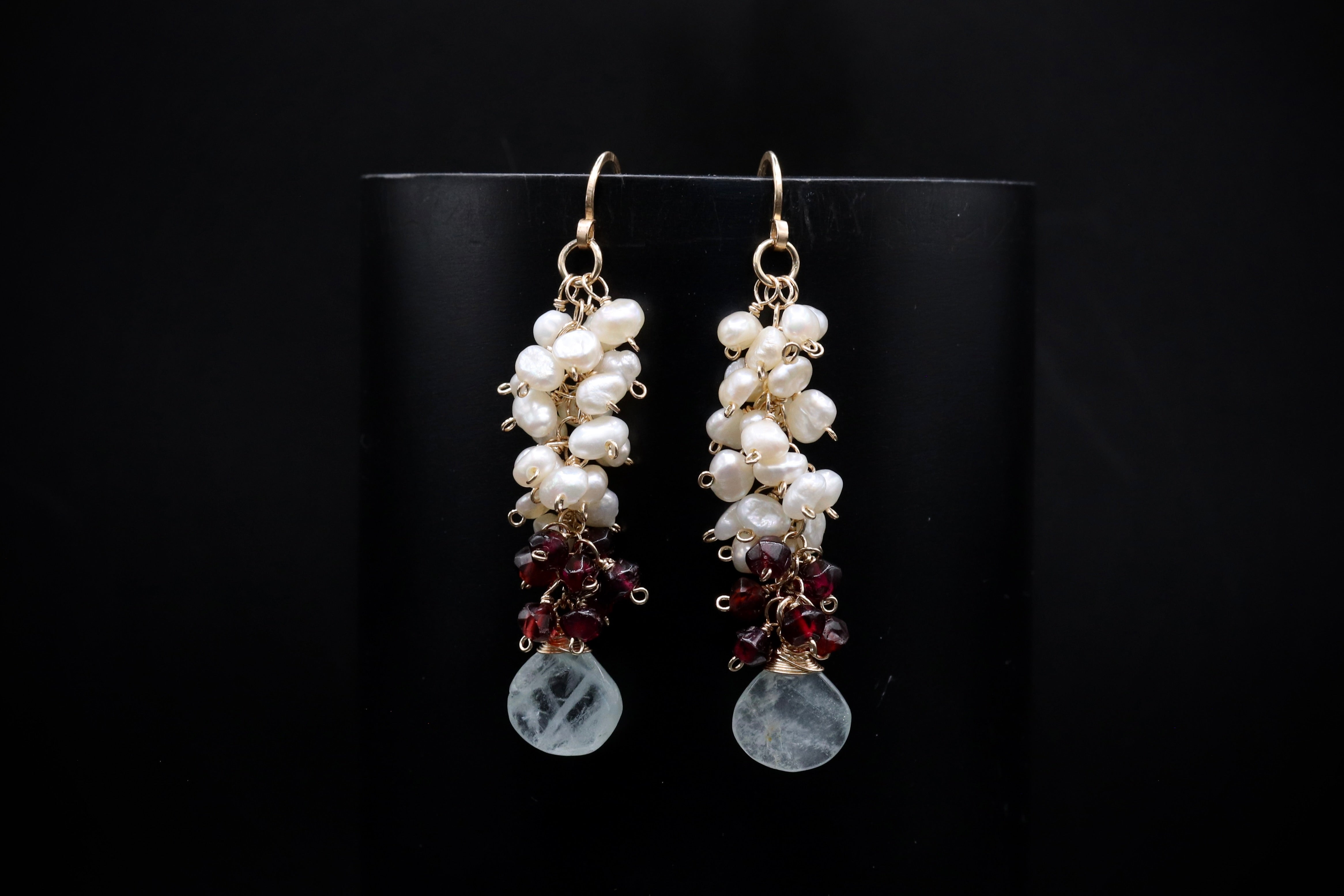 A pair of elegant earrings with white and maroon beads hanging from the bottom, set against a black background.