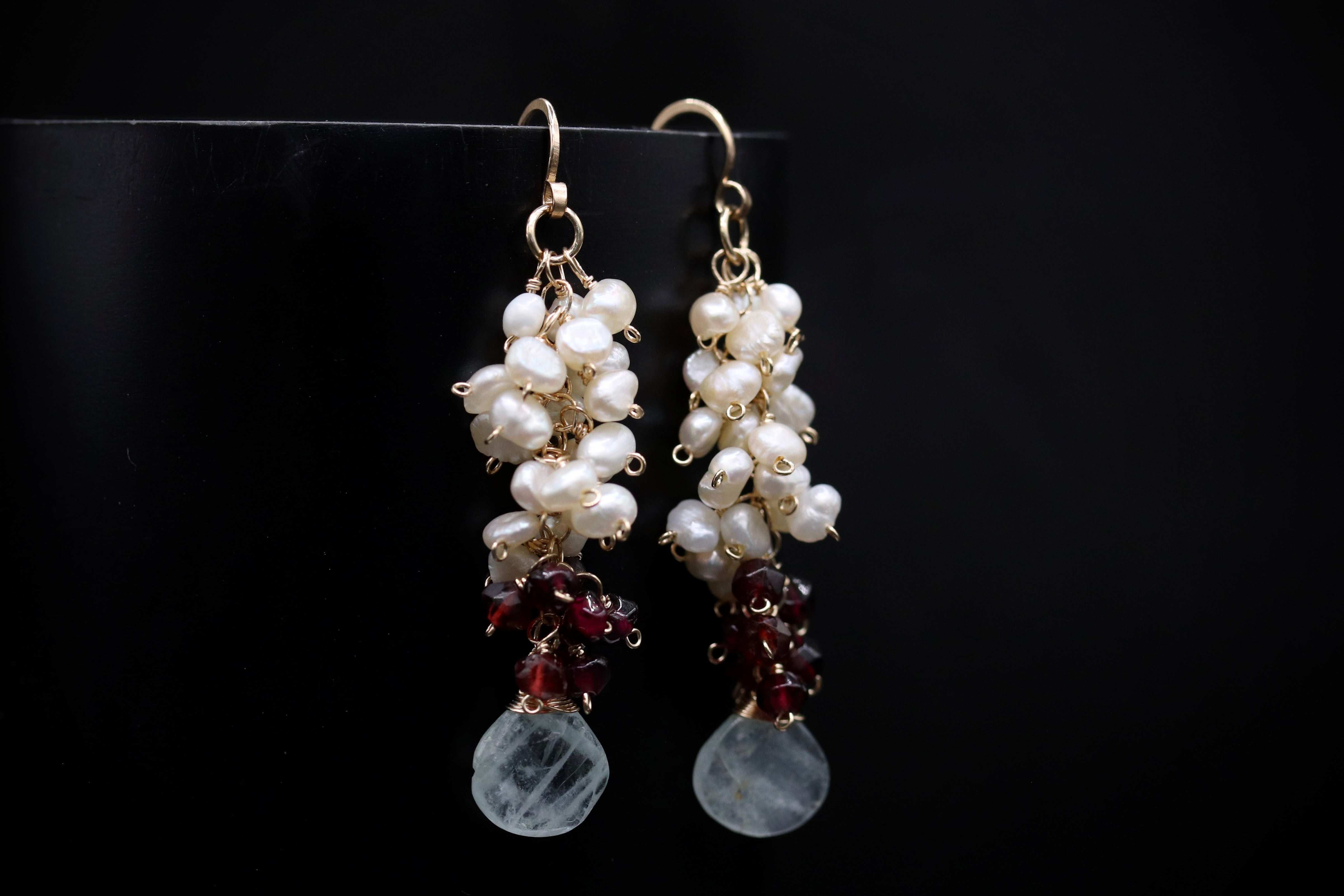 A pair of elegant earrings with white pearls and maroon gemstones hanging from the hooks against a black background.