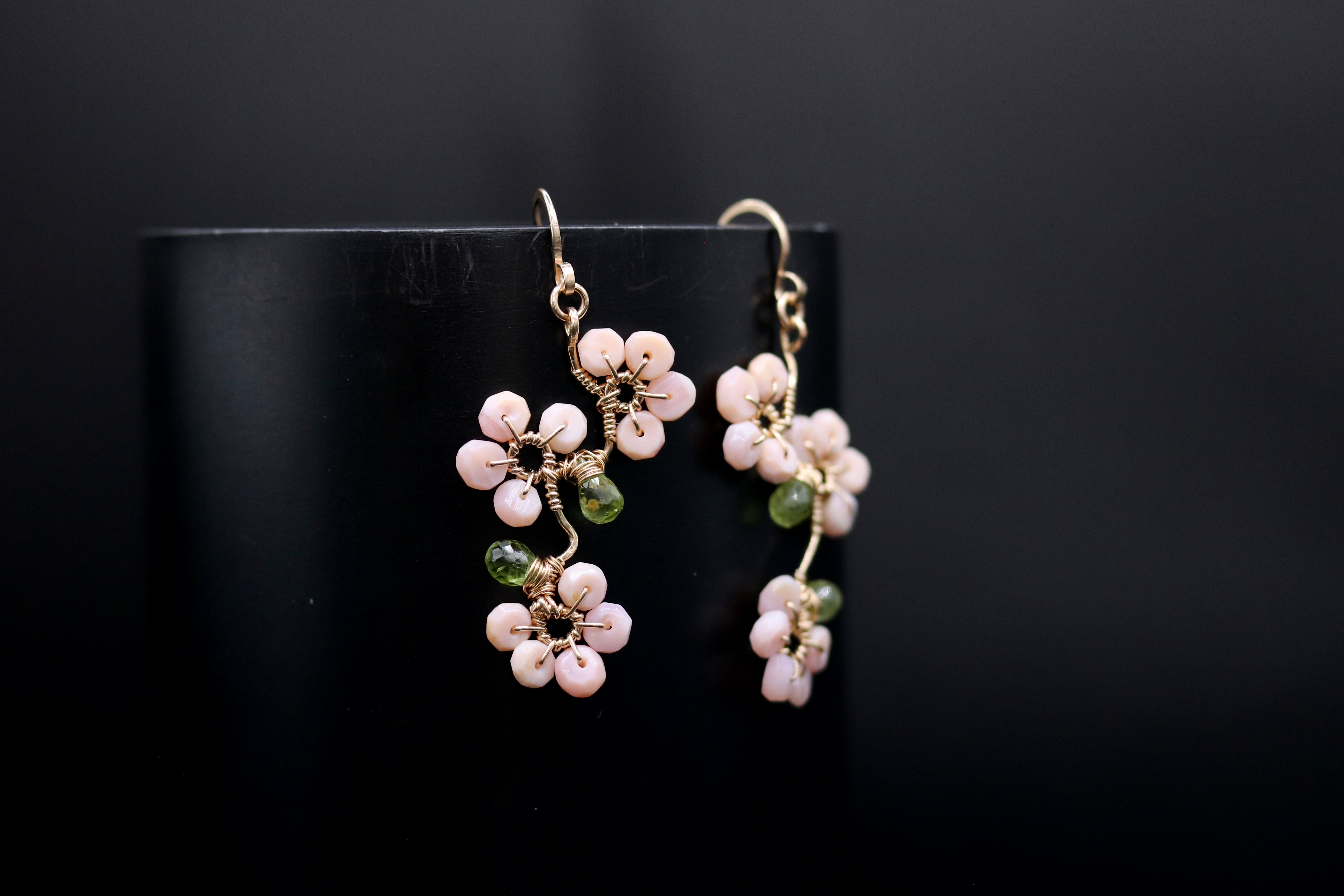 A pair of delicate earrings with white and green beads, resembling flowers, are displayed against a dark background.