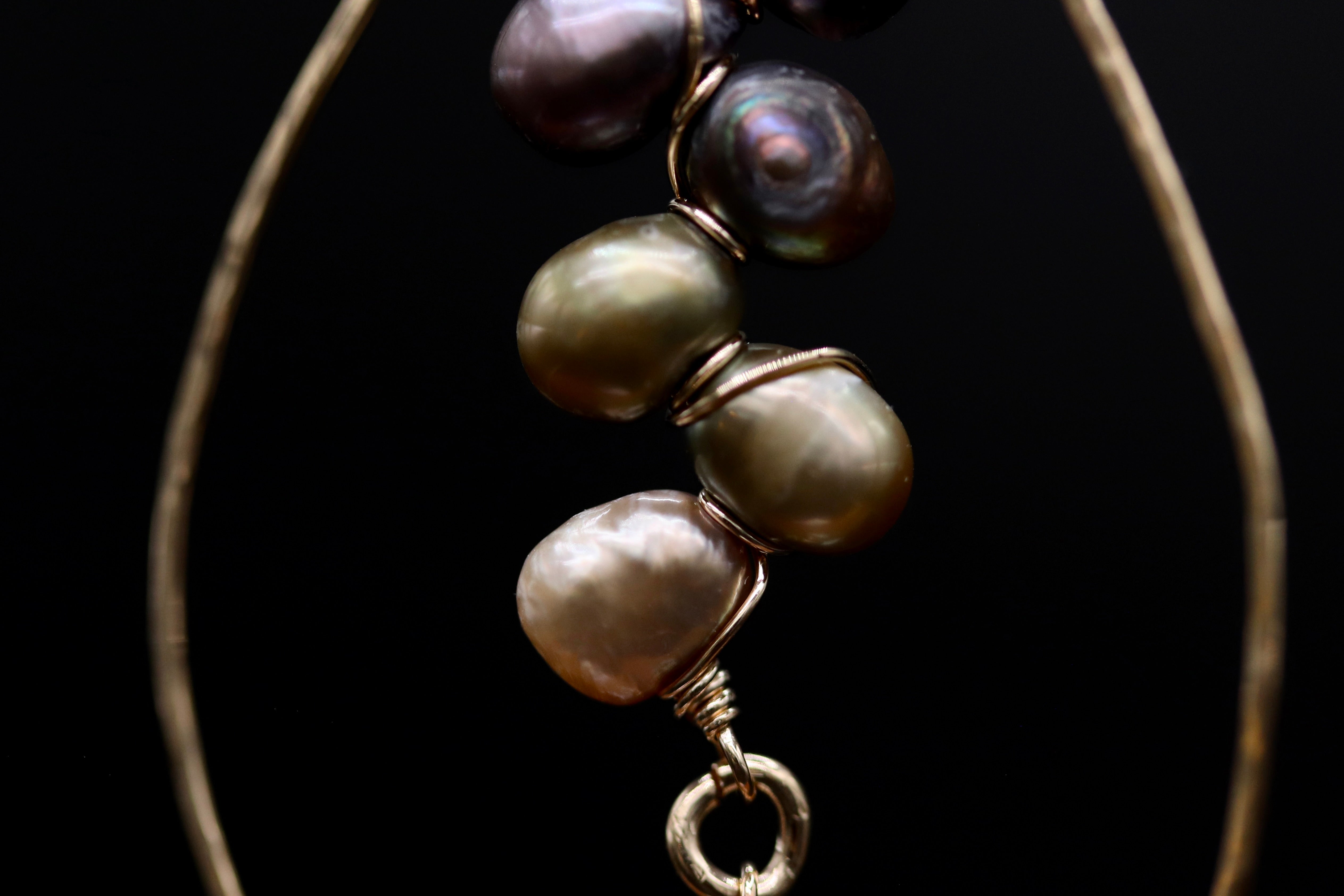 A close-up view of a gold-colored earring with a chain of pearls attached to it, set against a black background.