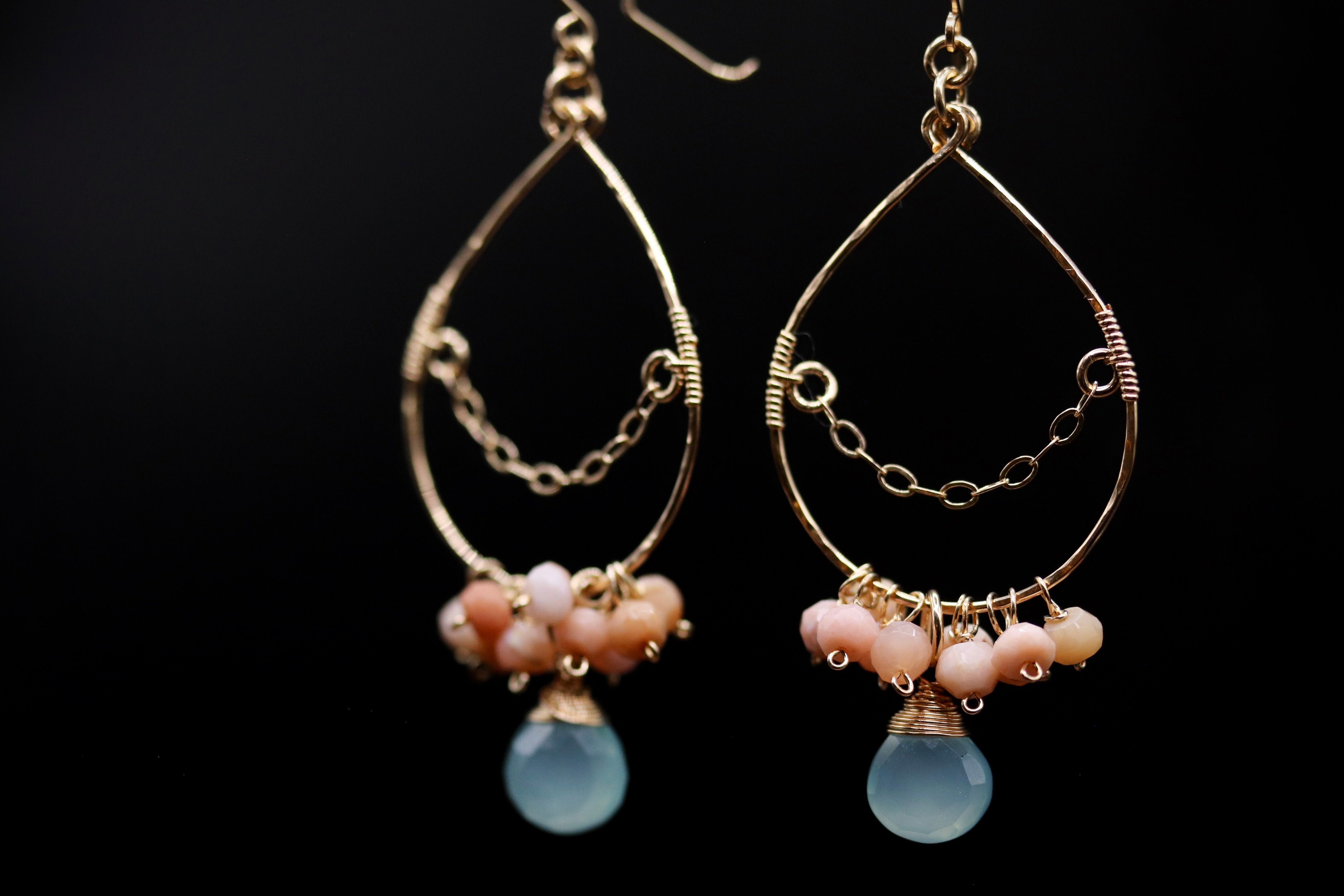 A pair of gold earrings with a teardrop-shaped design, featuring a blue gemstone and small beads in shades of pink and blue.