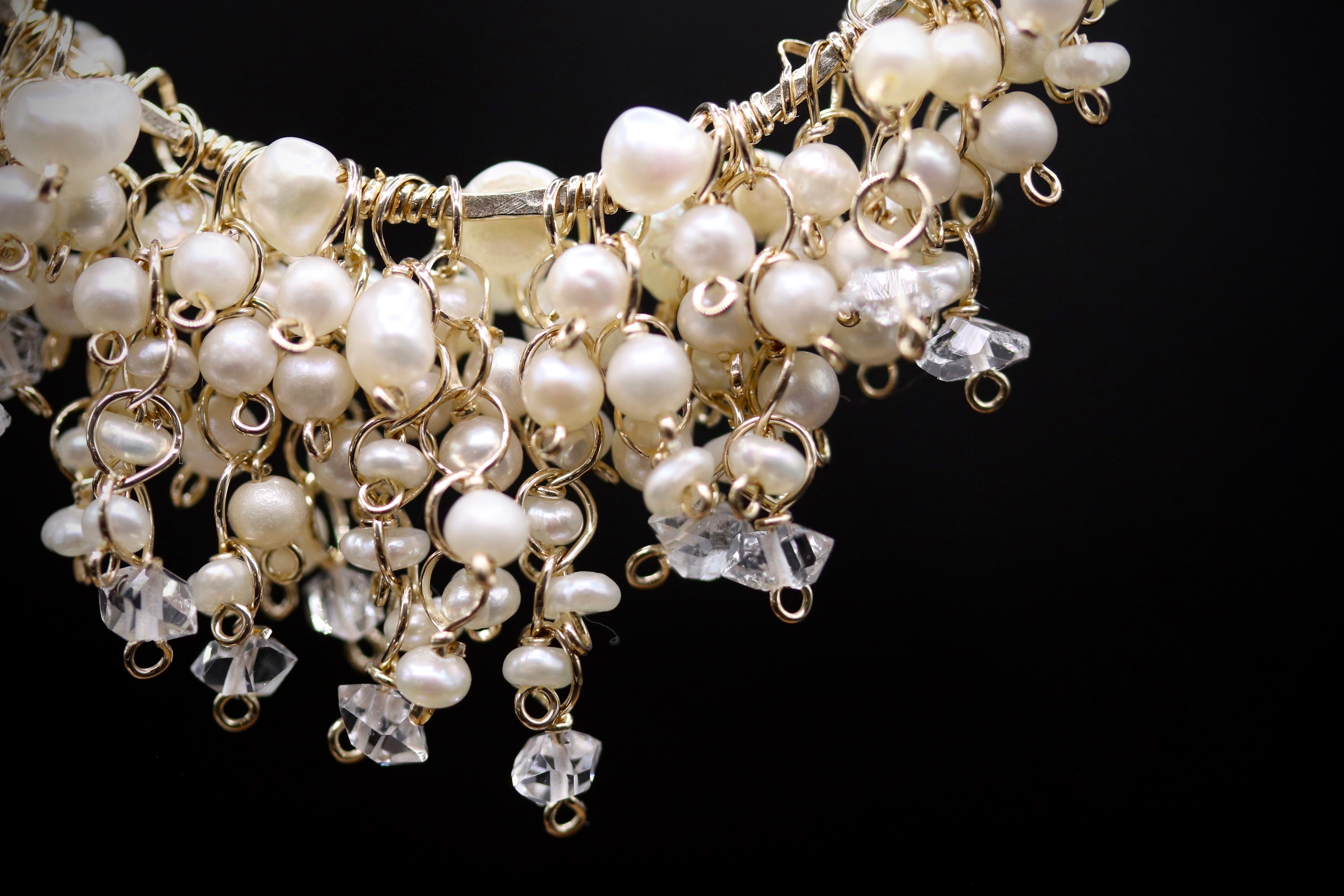 A close-up view of a delicate, ornate necklace with a combination of white pearls, clear crystals, and metal wire elements.