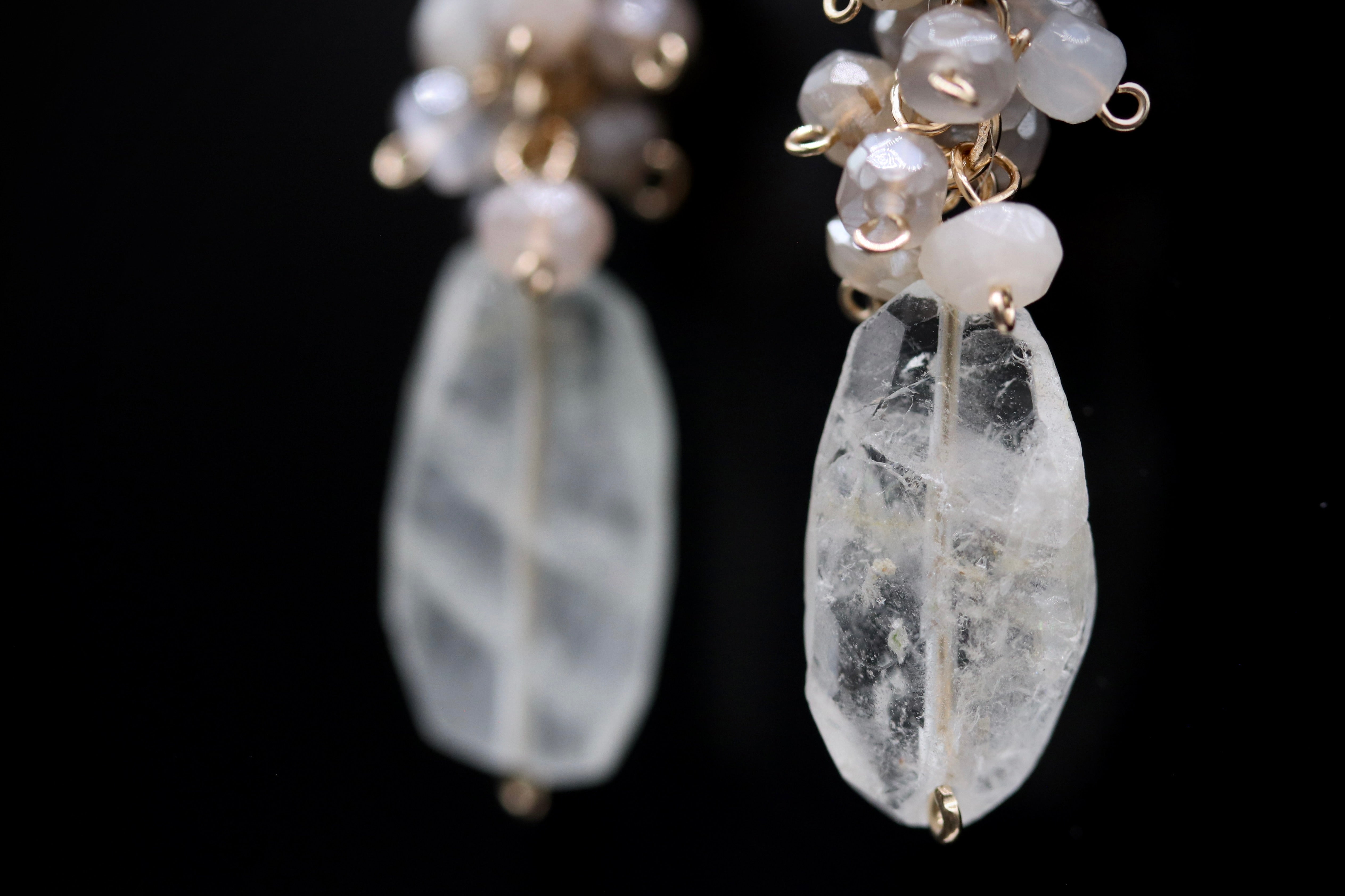 A close-up view of a pair of delicate earrings with clear crystal stones and gold-colored metal accents.