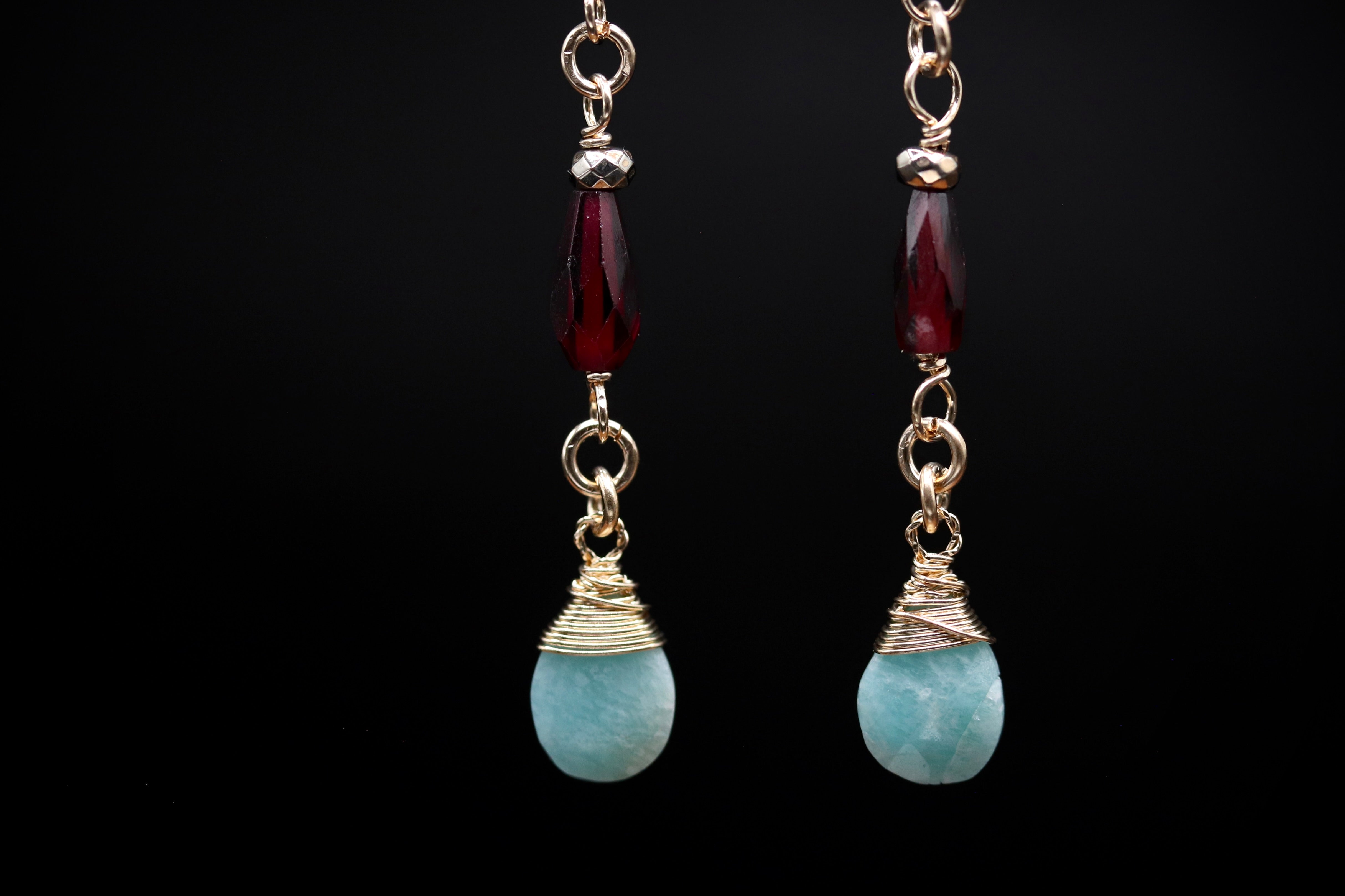 A pair of earrings with turquoise stones and red gemstones, suspended from gold chains against a black background.