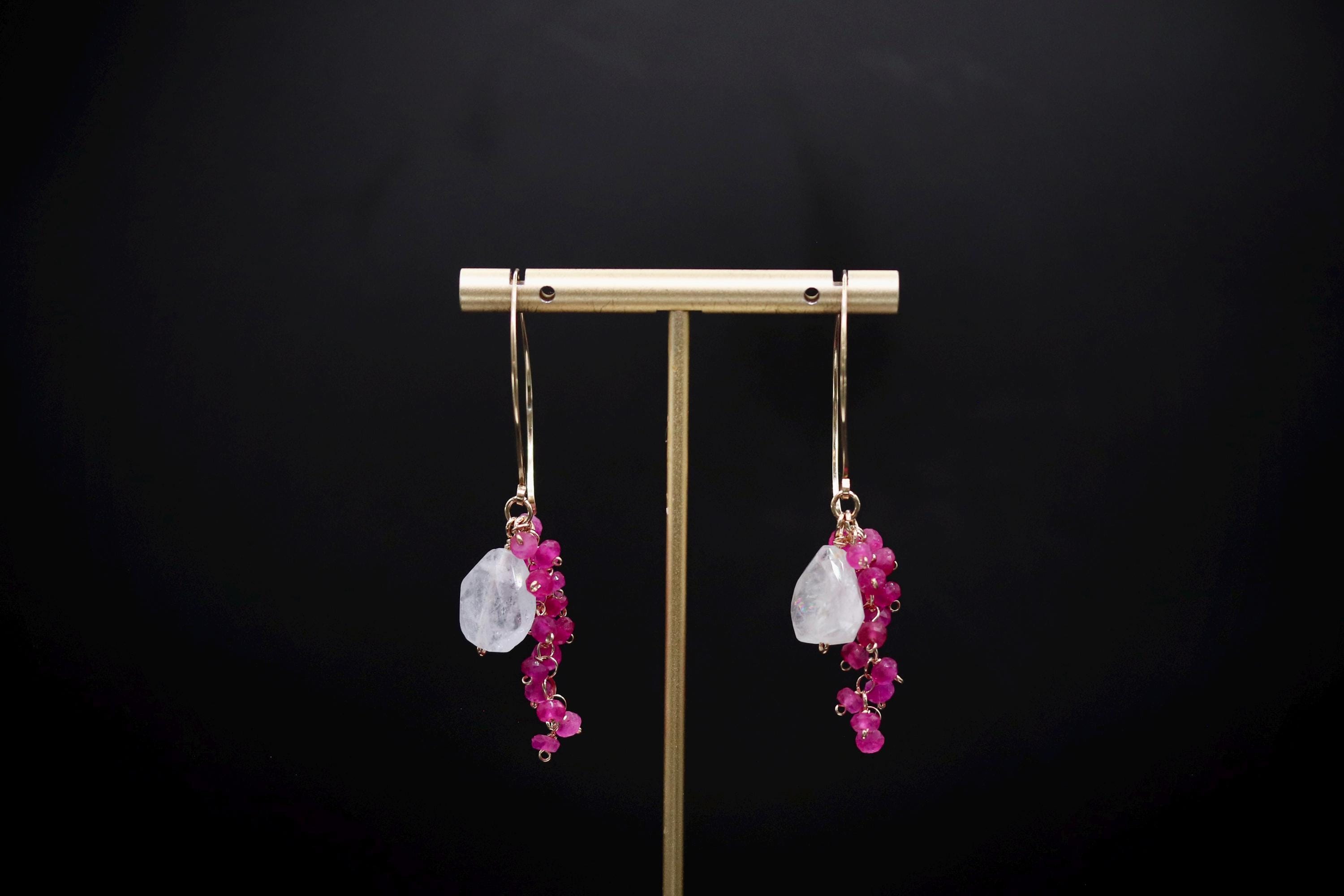 A pair of earrings with a gold-colored metal stand and hanging earrings with a combination of pink and white stones and red gemstones.