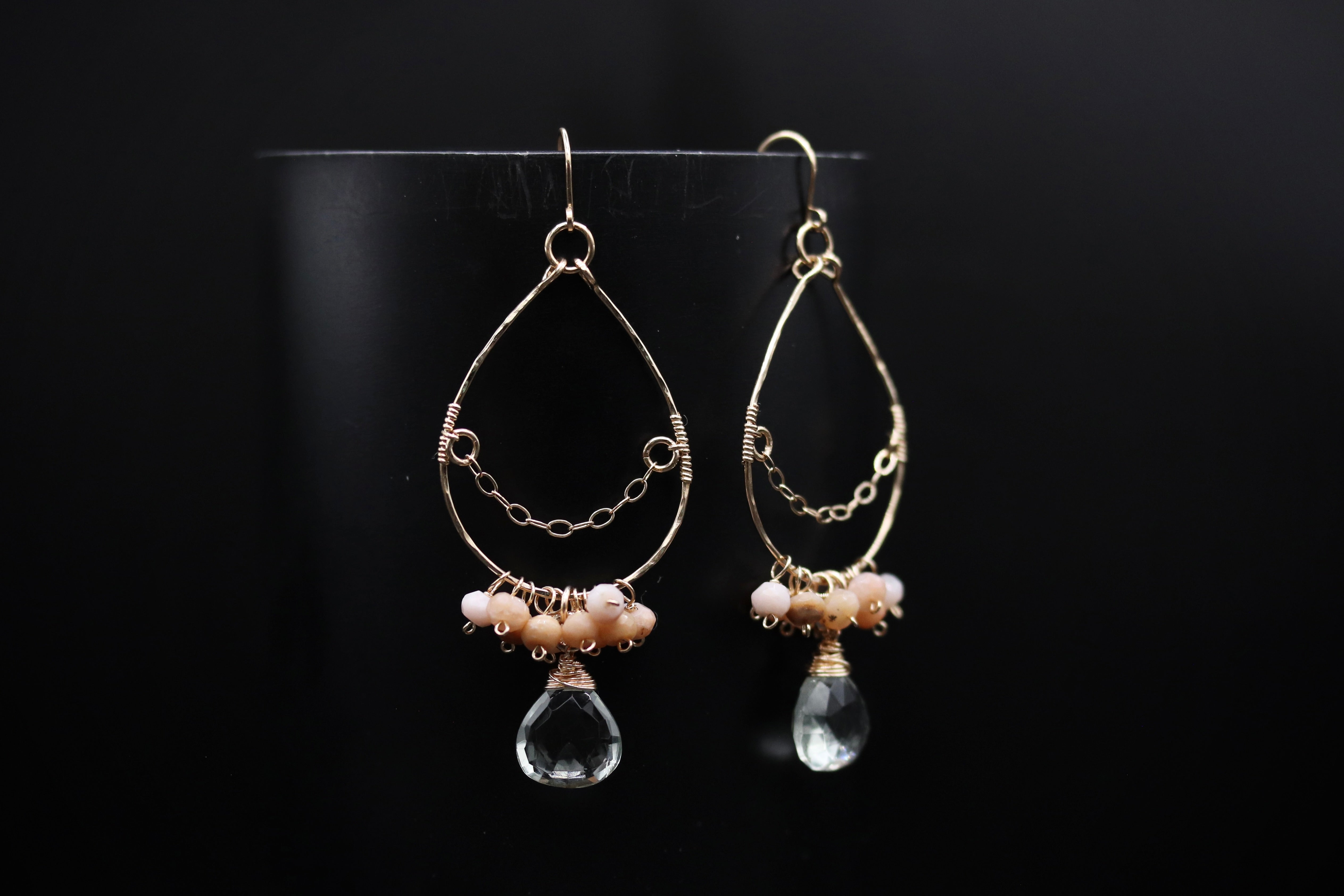 A pair of elegant earrings with a clear crystal pendant and beaded accents, displayed against a black background.