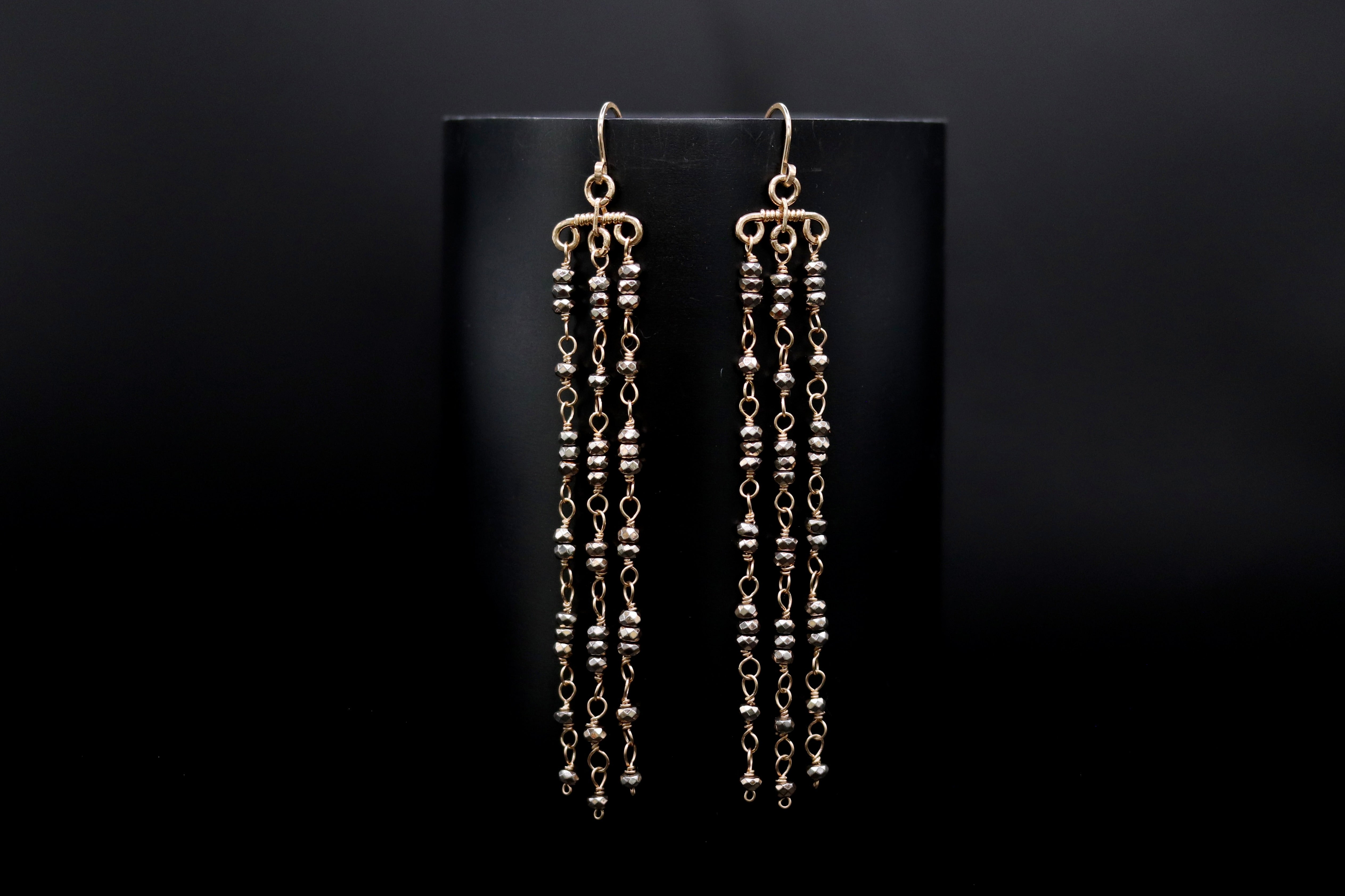 A pair of gold earrings with long, dangling chains and small beads hanging from them, displayed against a black background.