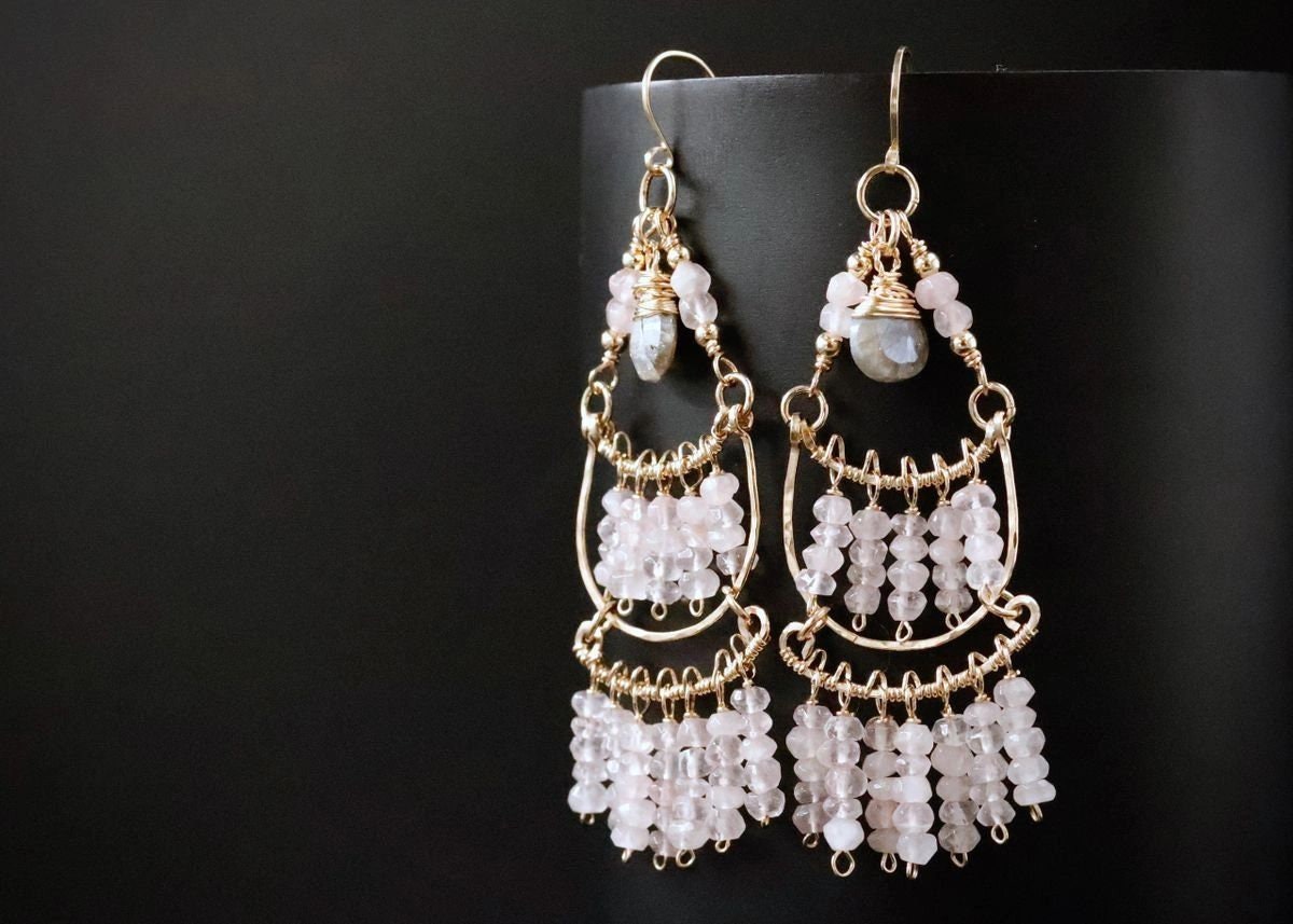 May include: Gold dangle earrings with multiple tiers of pink and white beads and a larger, teardrop-shaped stone at the top.