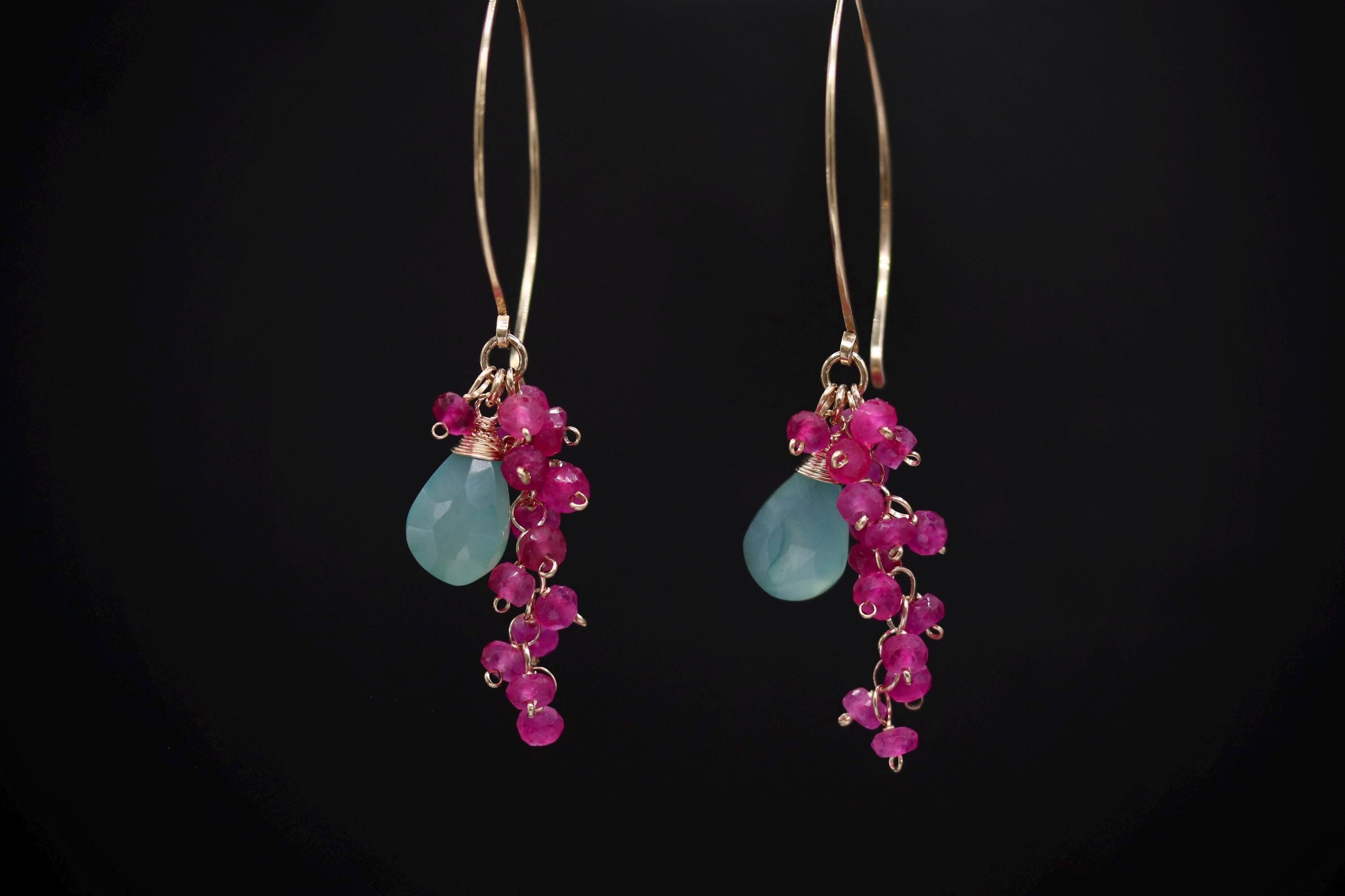 A pair of earrings with a combination of blue and pink gemstones, as well as small pink beads, hanging from a gold hoop.