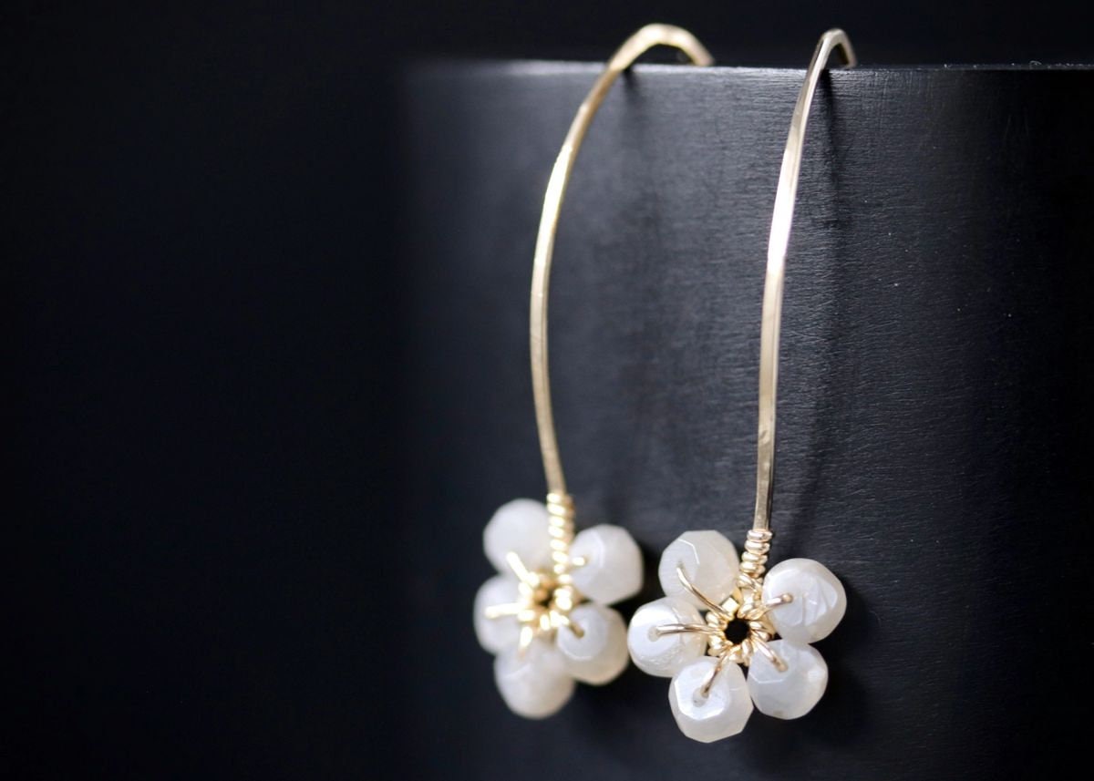 May include: A pair of gold dangle earrings with white gemstone flower accents.