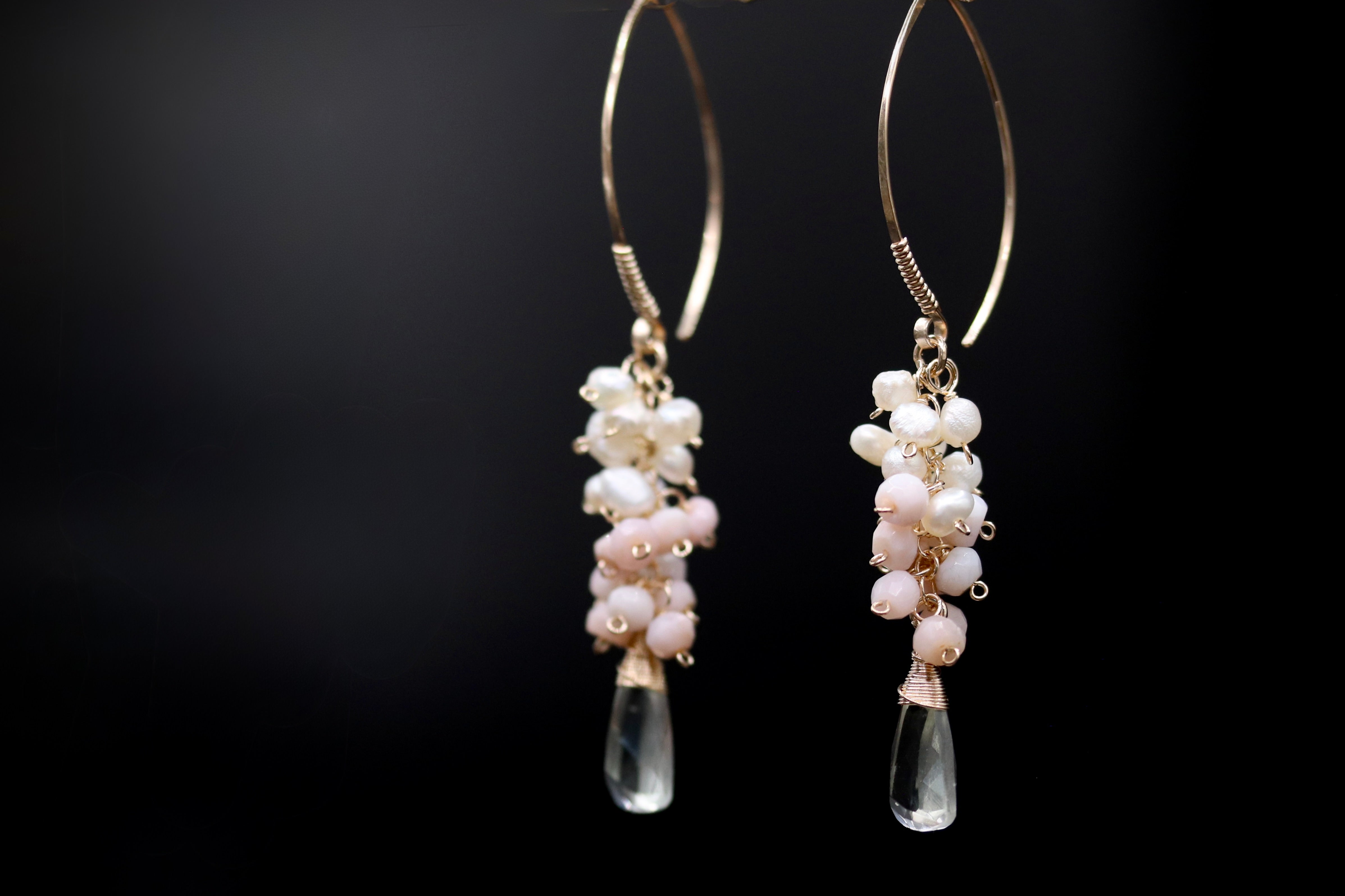 A pair of elegant earrings with clear beads and white pearls hanging from the hooks against a dark background.