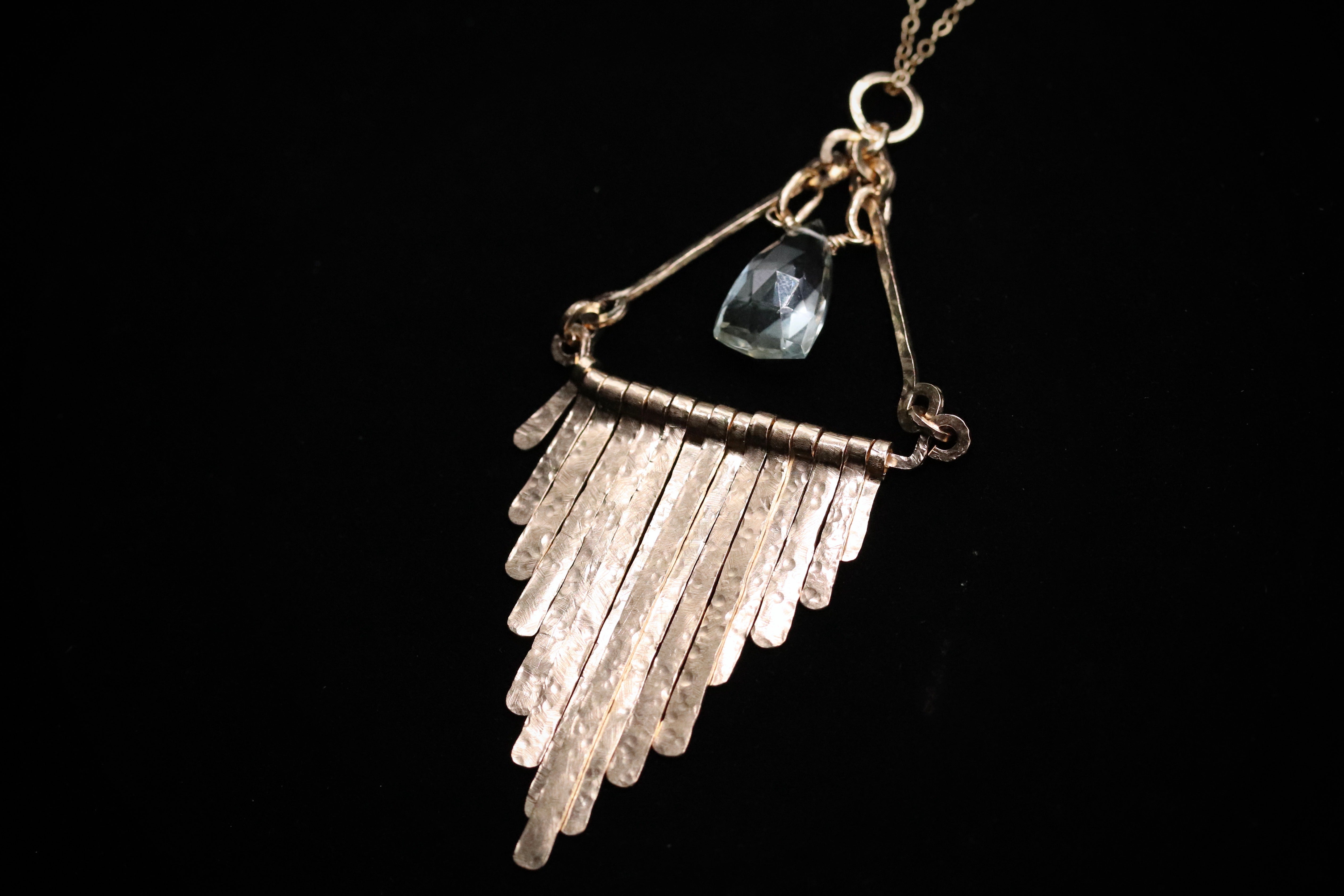 A silver necklace with a pendant featuring a clear gemstone, hanging against a black background.