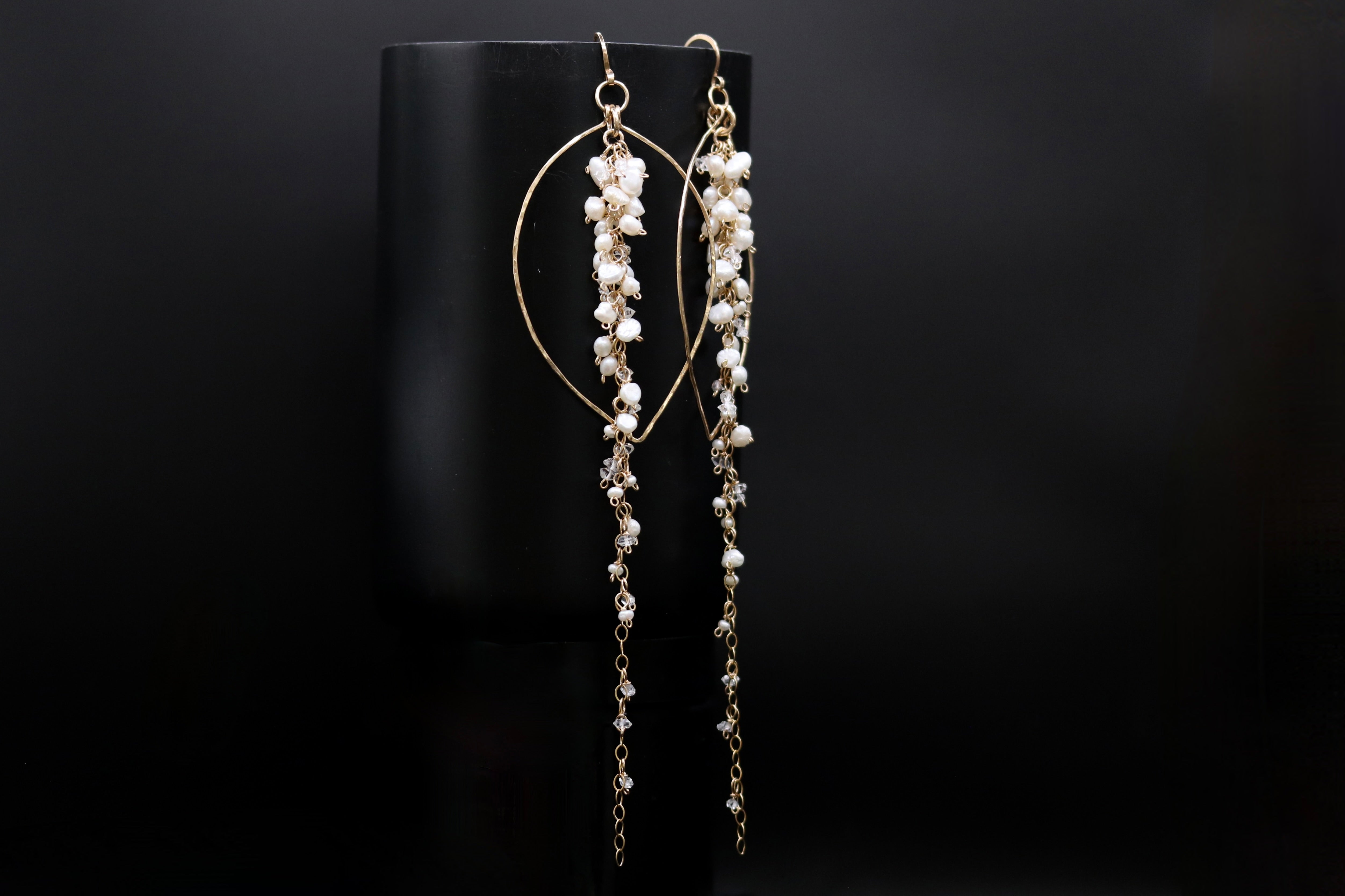 A pair of elegant gold earrings with long, dangling pearls and a circular design, displayed against a black background.