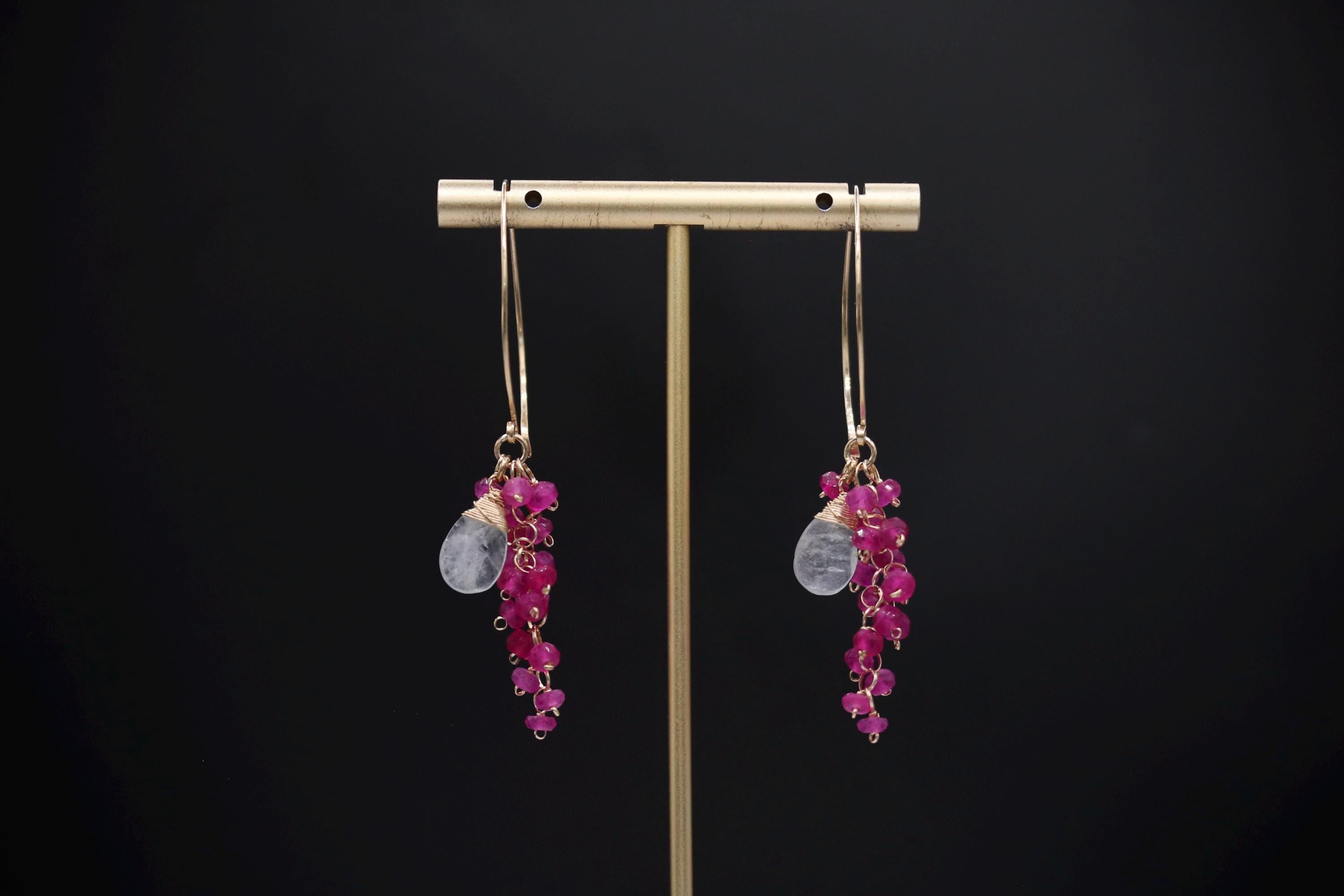 A pair of earrings with a gold-colored metal stand and hanging earrings adorned with small, colorful stones.