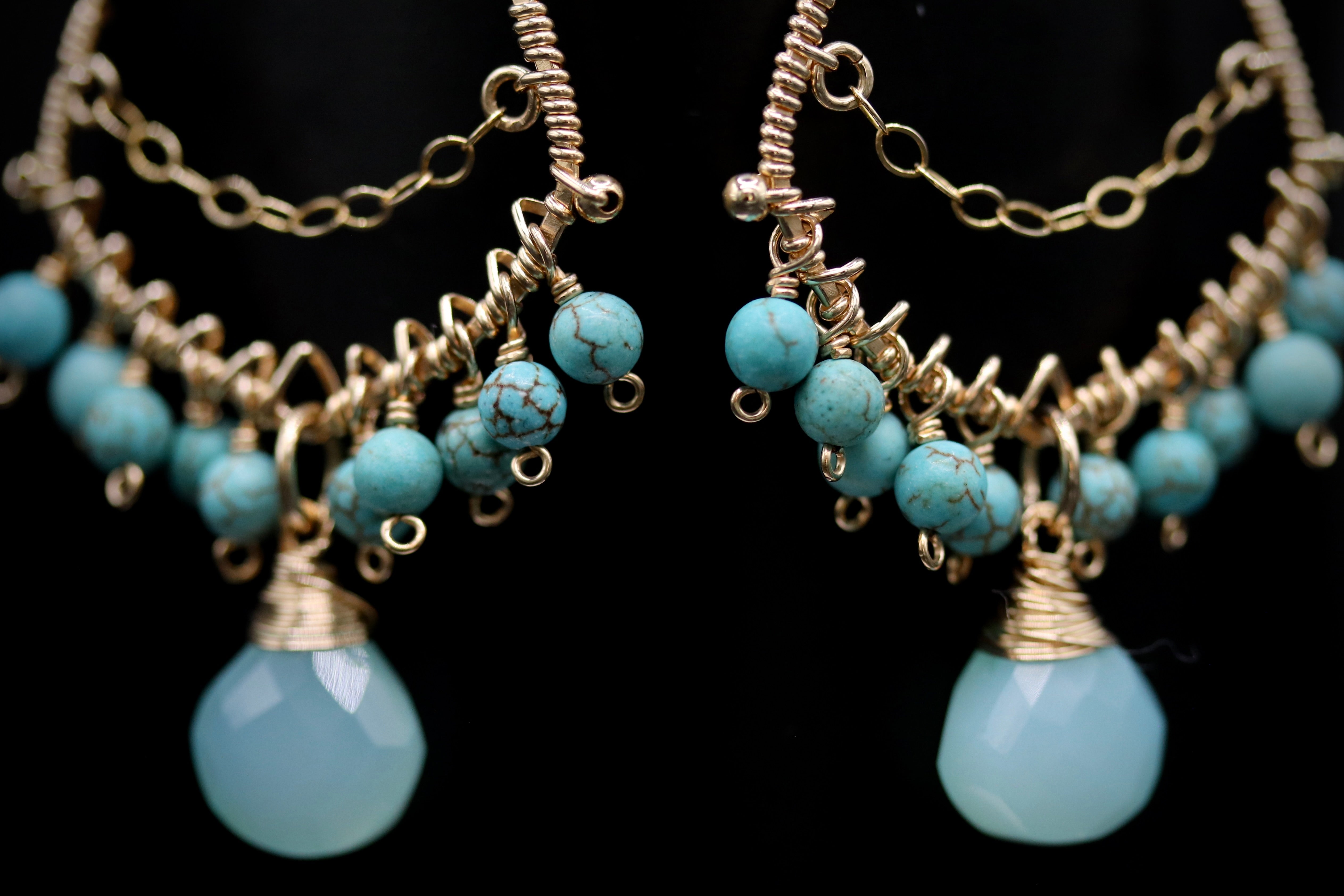 A pair of ornate earrings with turquoise beads and gold-colored metal chains.