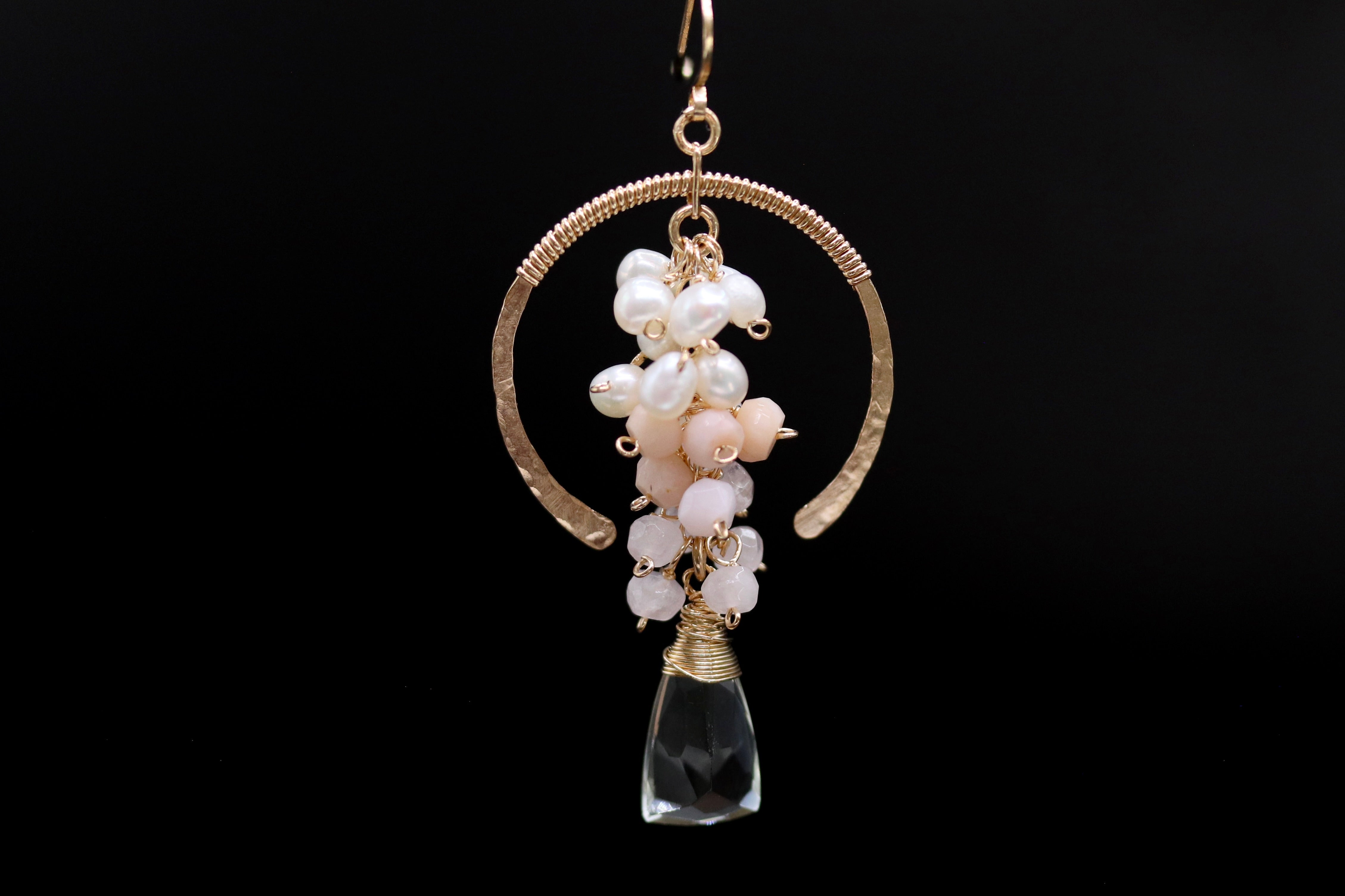 A pair of earrings with a clear gemstone and a cluster of white and pink pearls hanging from a gold-colored metal frame.