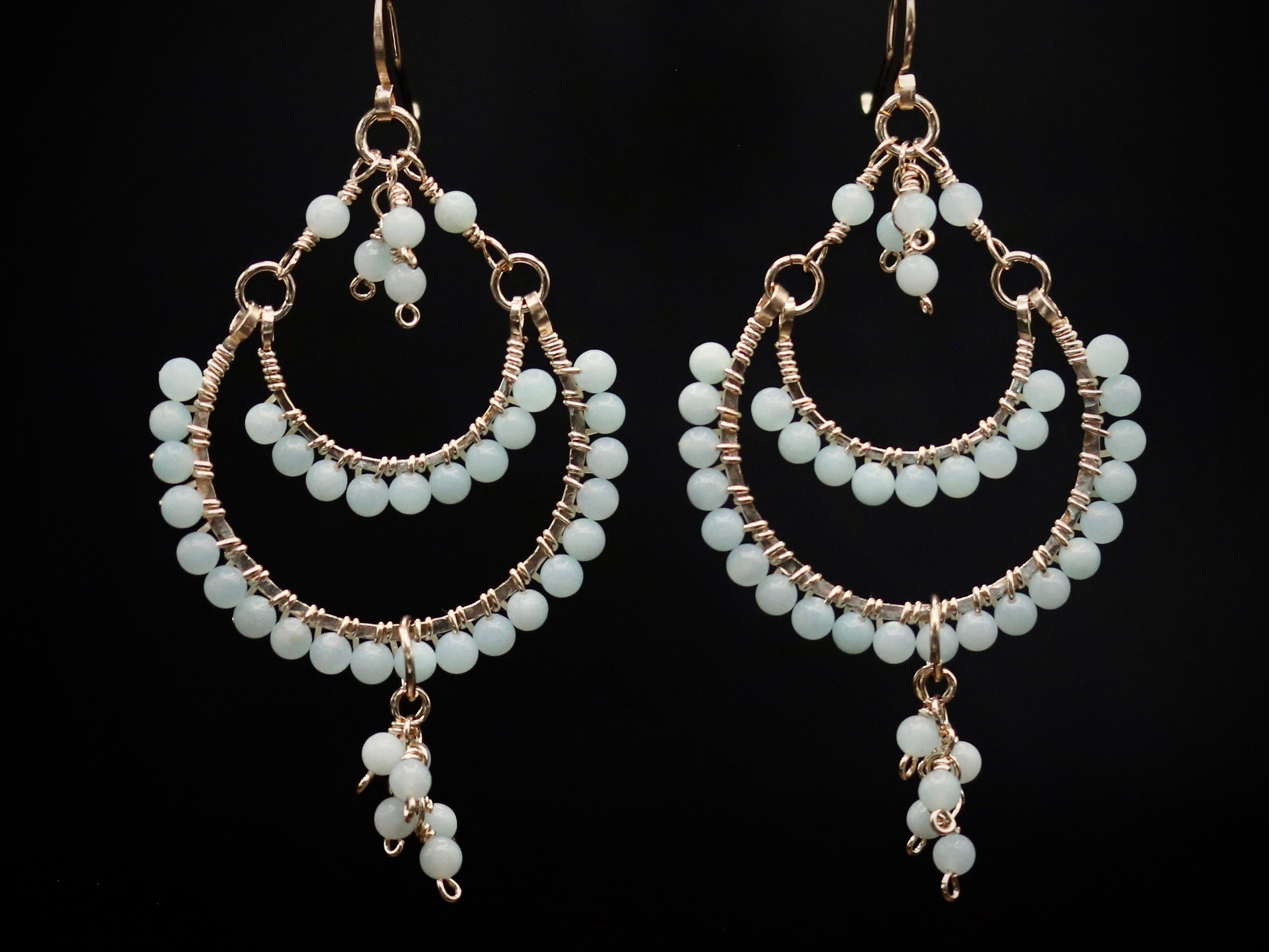 A pair of elegant earrings with white beads and dangling charms against a black background.