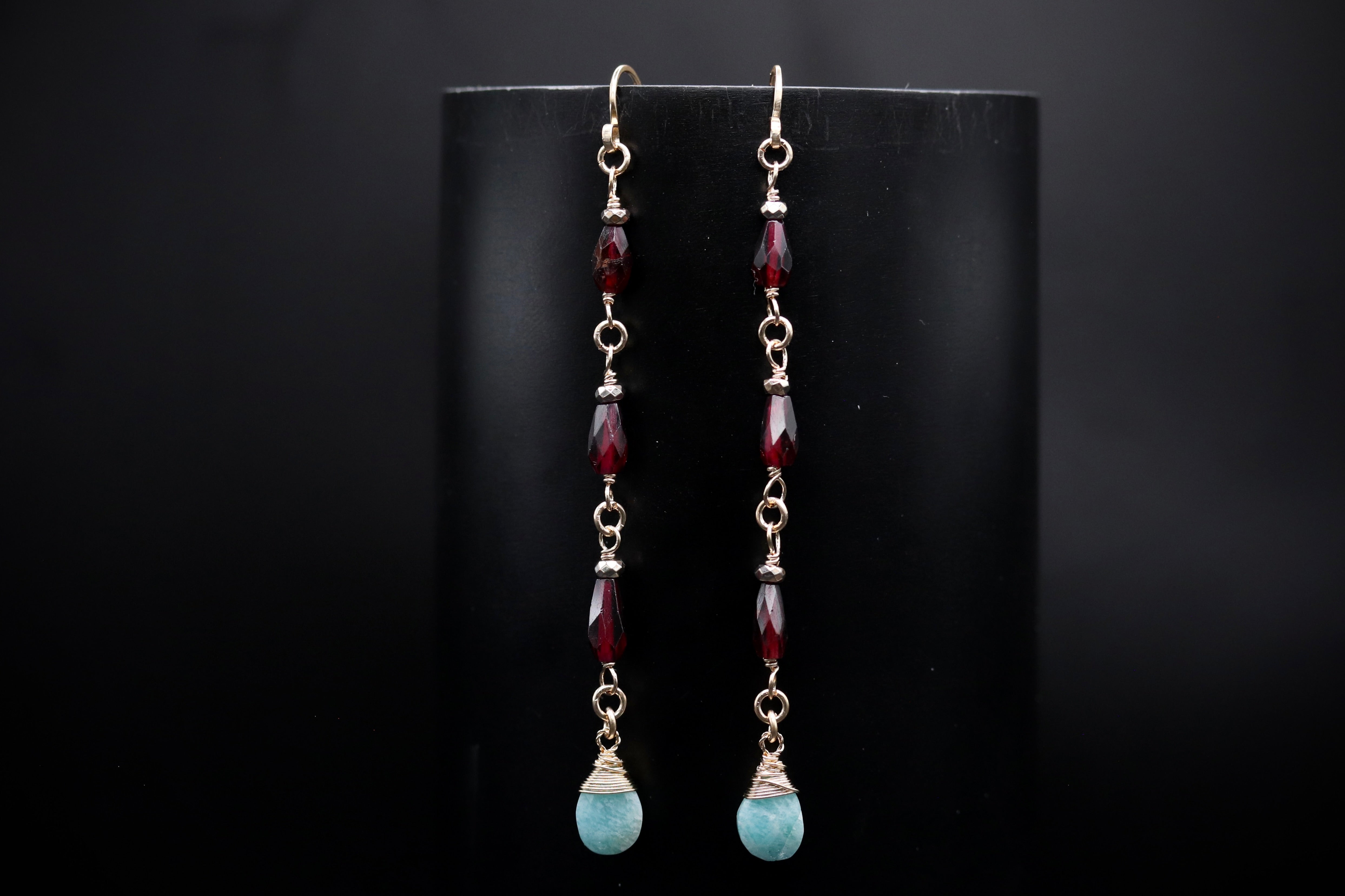 A pair of earrings with red gemstones and aquamarine stones, hanging from a black background.