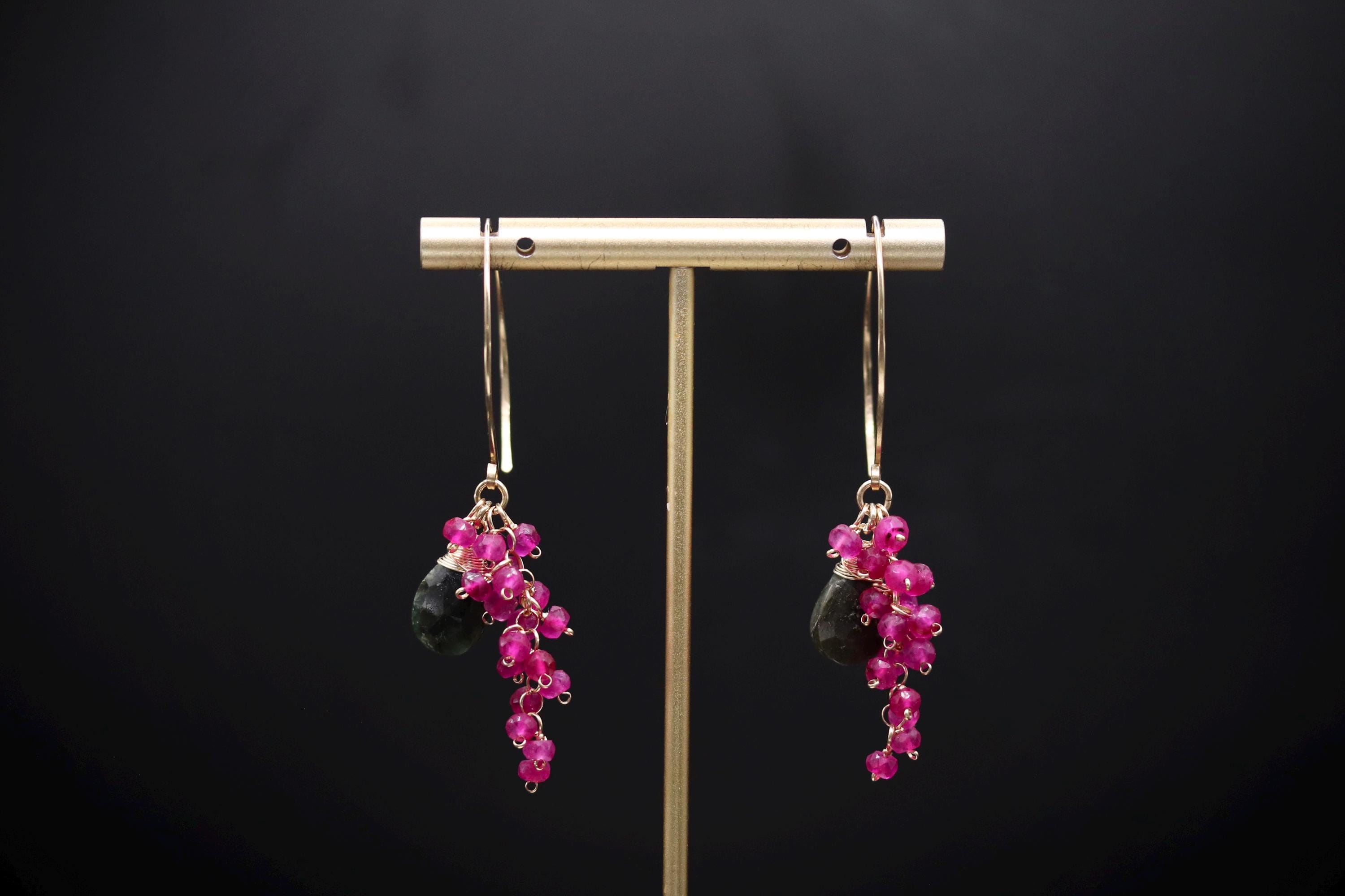 A pair of earrings with a gold-colored metal stand and dangling earrings with pink gemstones.