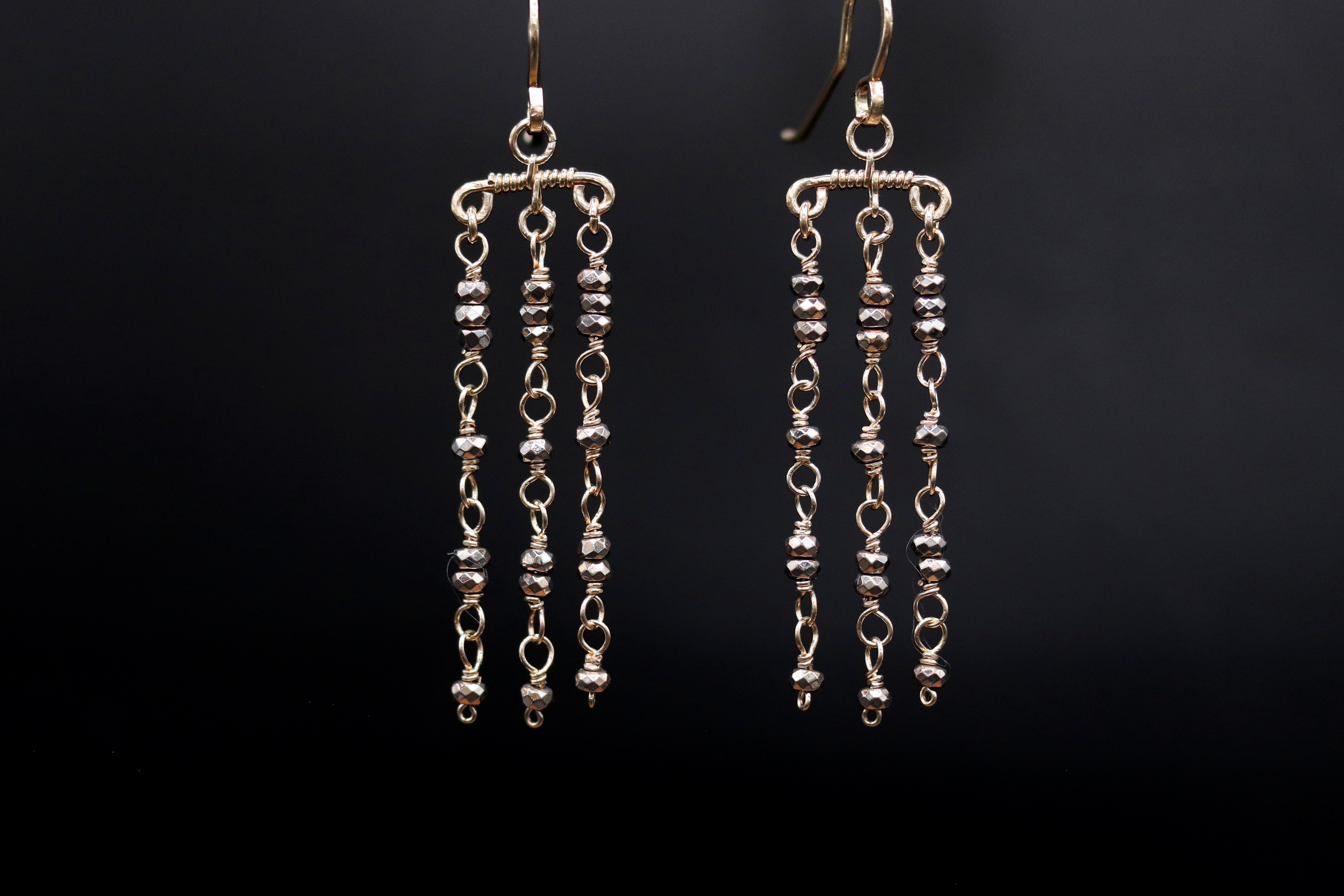 A pair of gold earrings with dangling beads hanging from the hooks against a dark background.