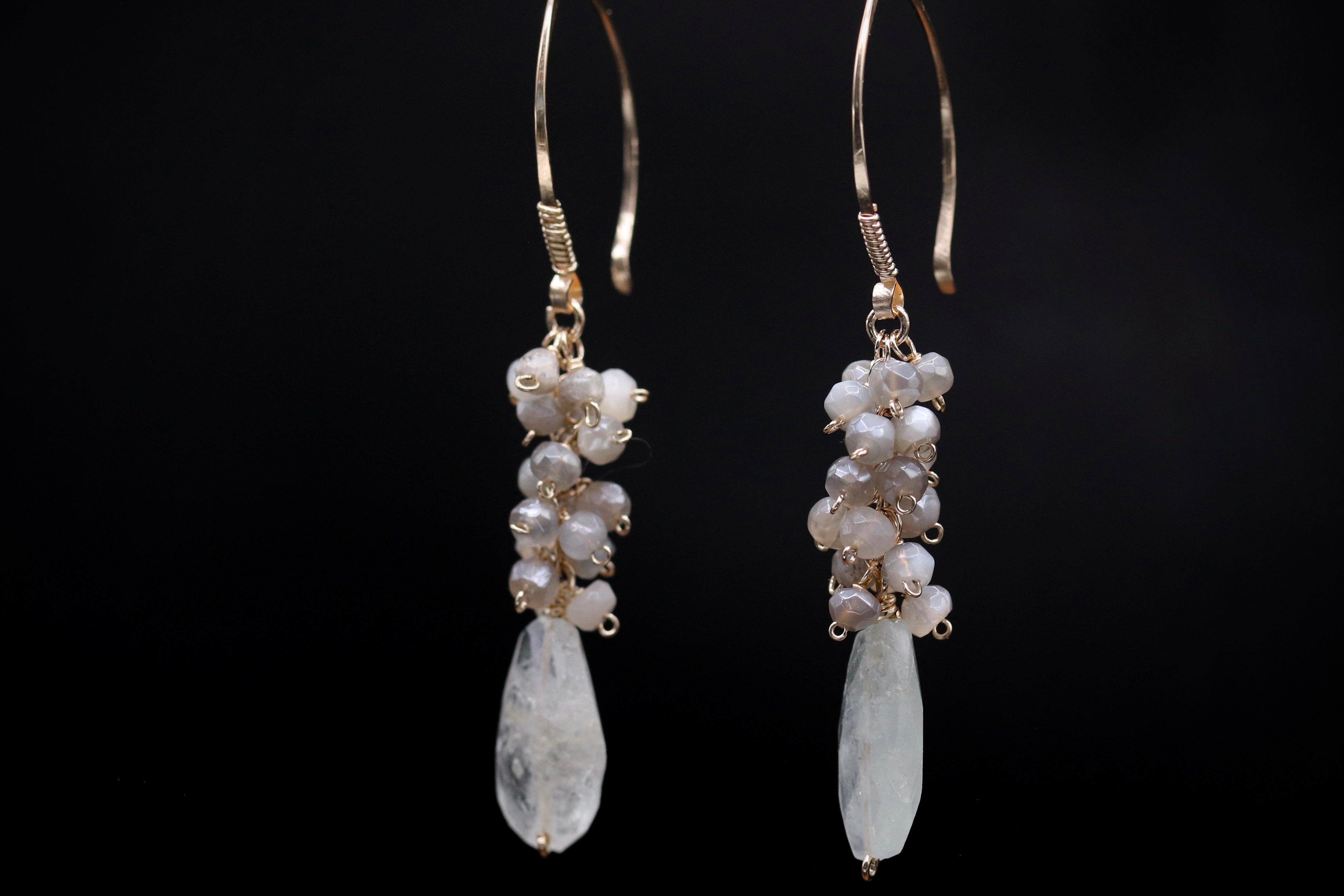 A pair of elegant earrings with white stones and dangling gold hooks against a black background.