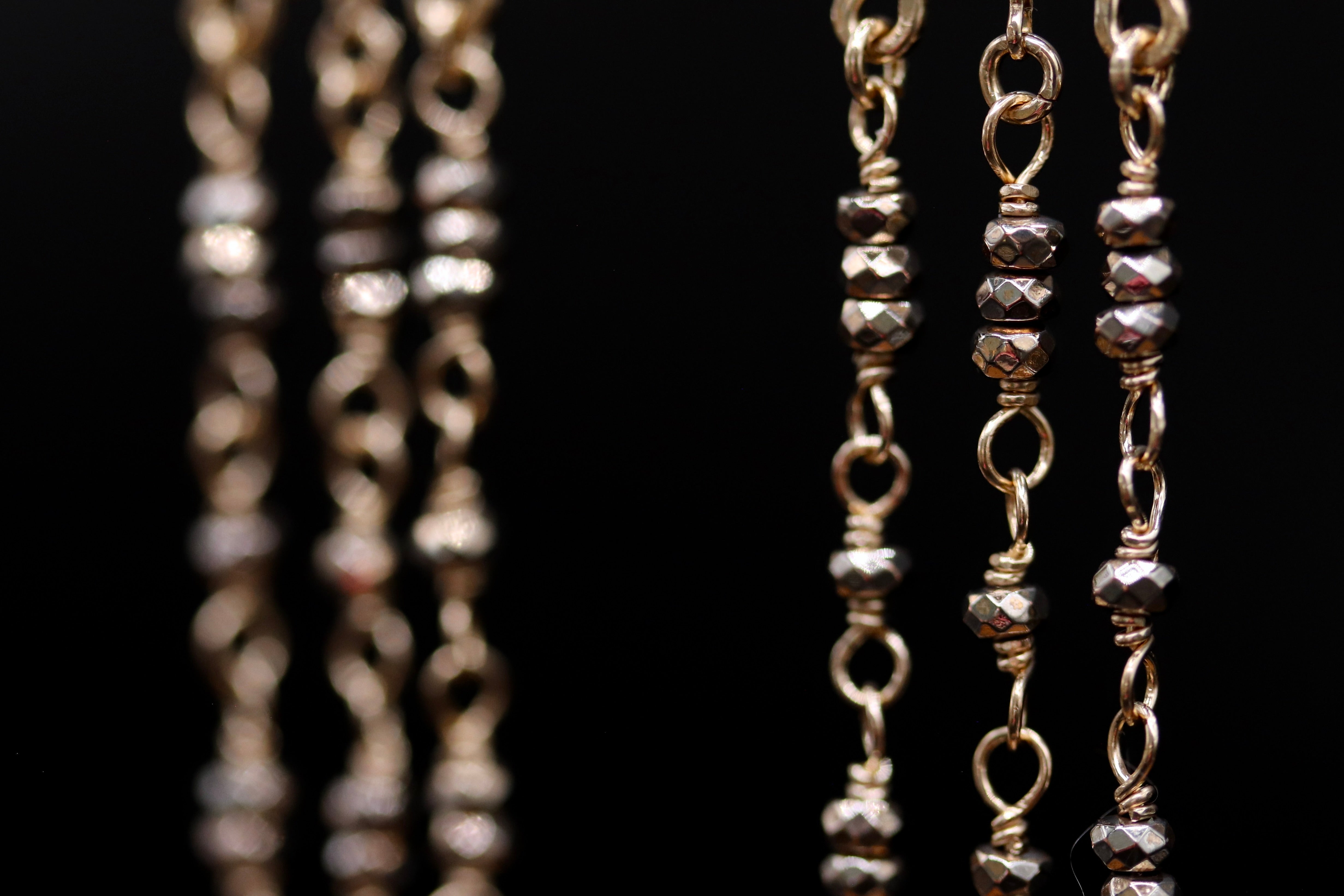 A close-up view of a chain with small, shiny metal beads attached to it, set against a black background.