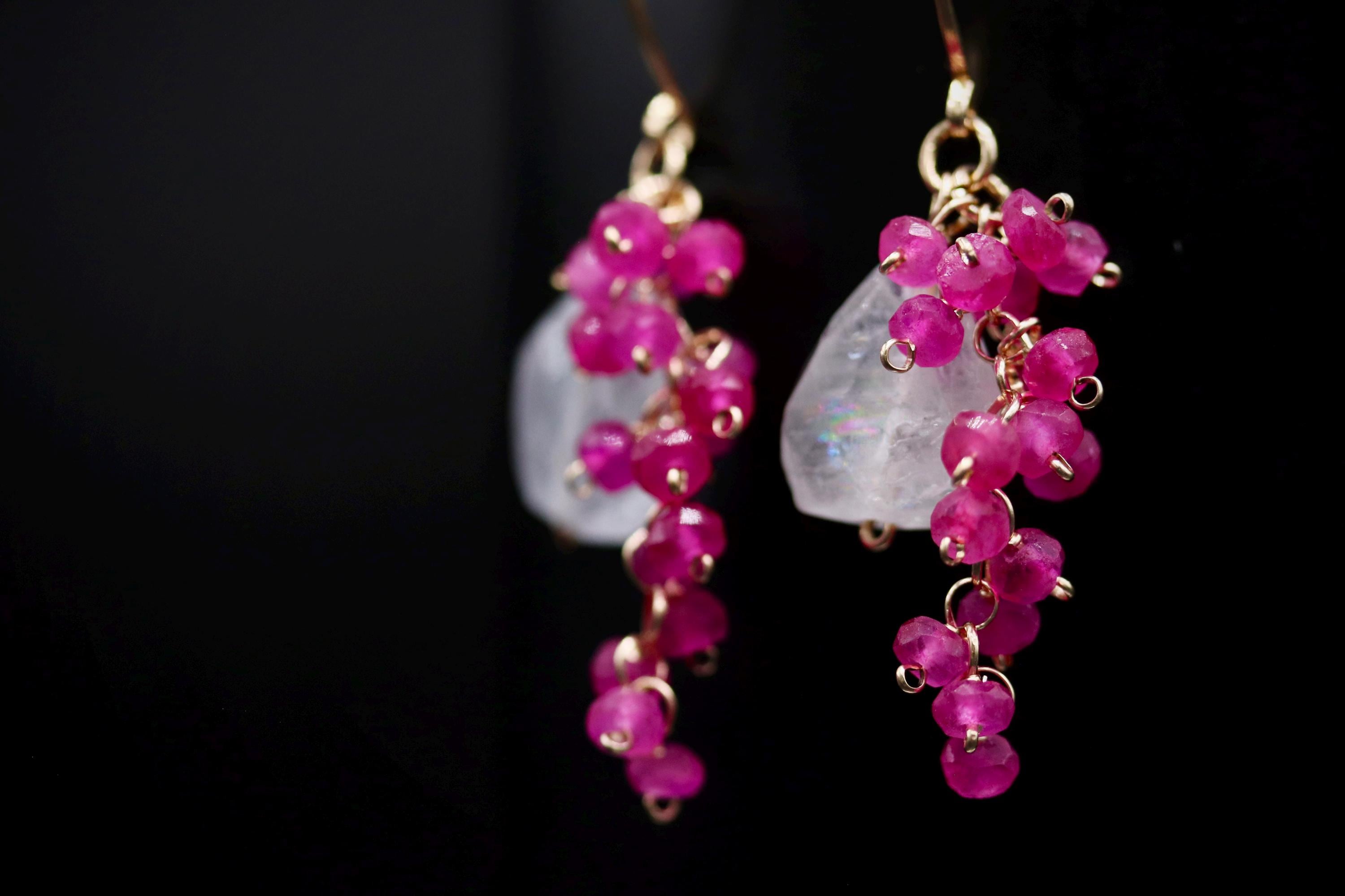 A pair of elegant earrings with a combination of pink and clear gemstones, creating a striking contrast against the dark background.