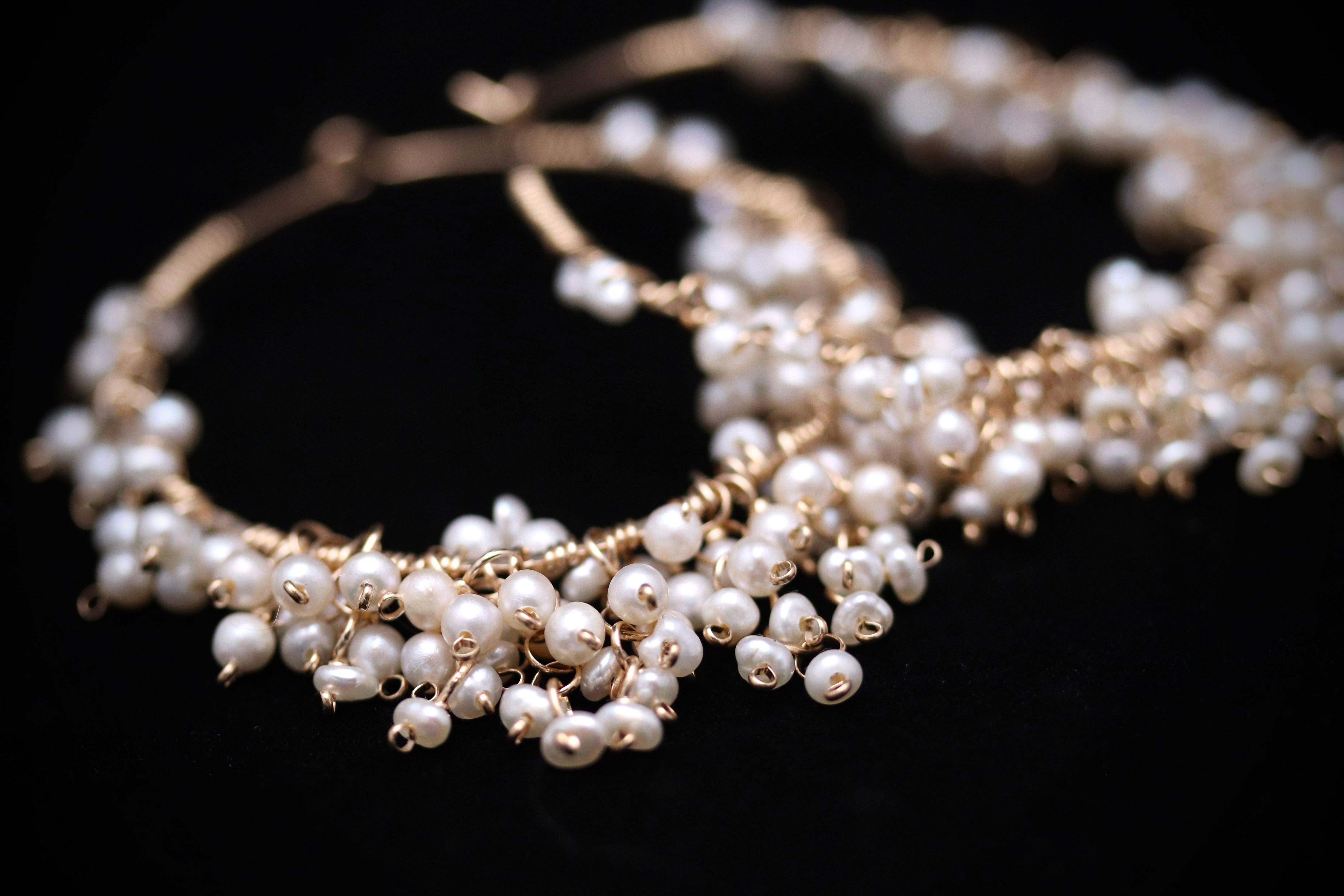 A close-up image of a delicate, ornate necklace made of small, white pearls with a metallic, dangling design.