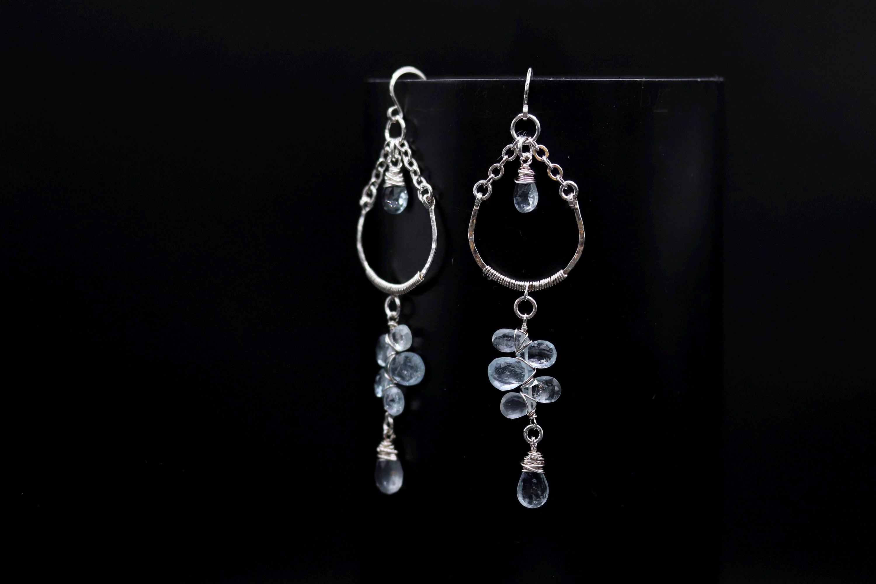 A pair of elegant silver earrings with dangling clear gemstone accents, displayed against a black background.