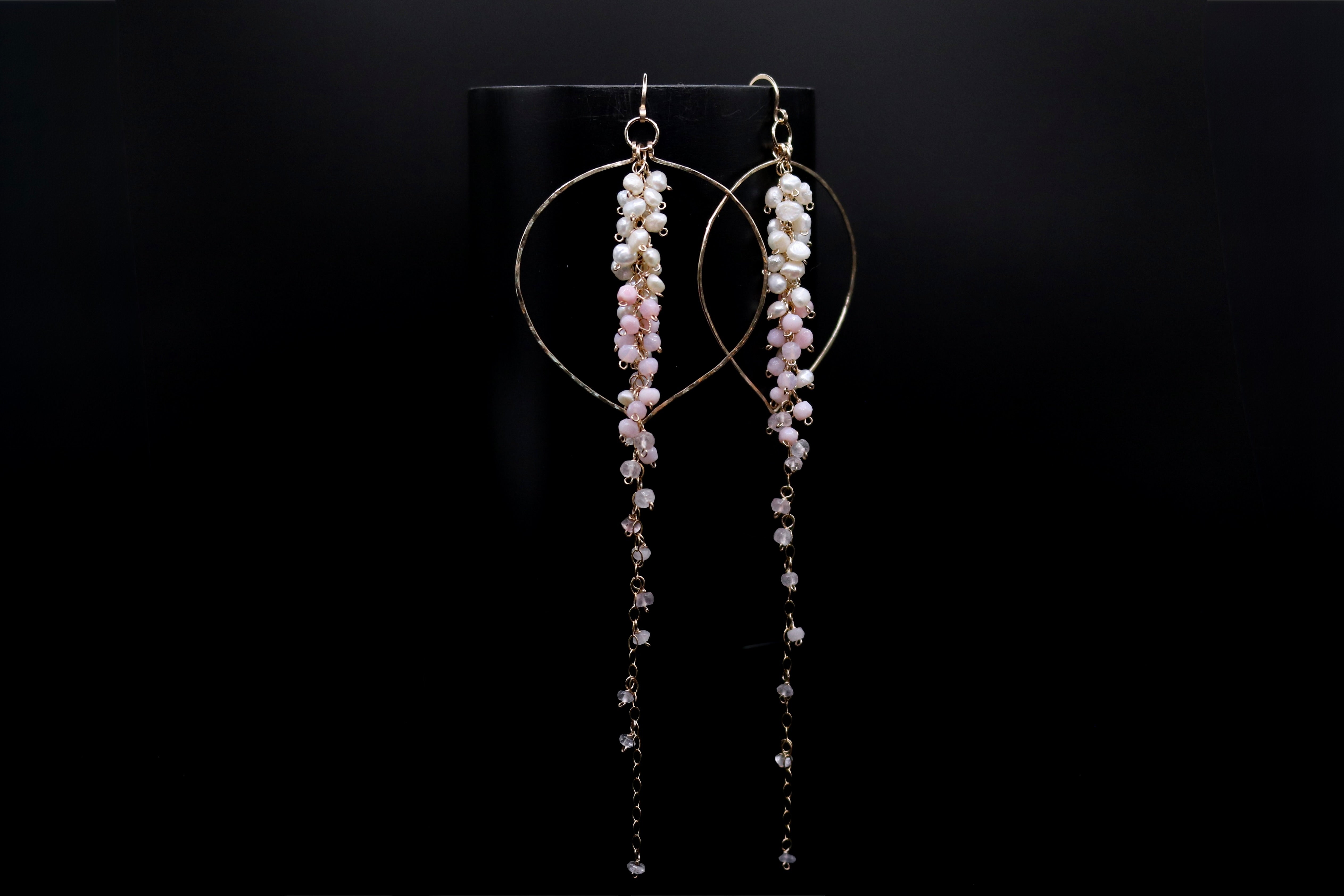A pair of elegant earrings with long, dangling strands of small, white beads or pearls hanging from a circular metal frame against a black background.