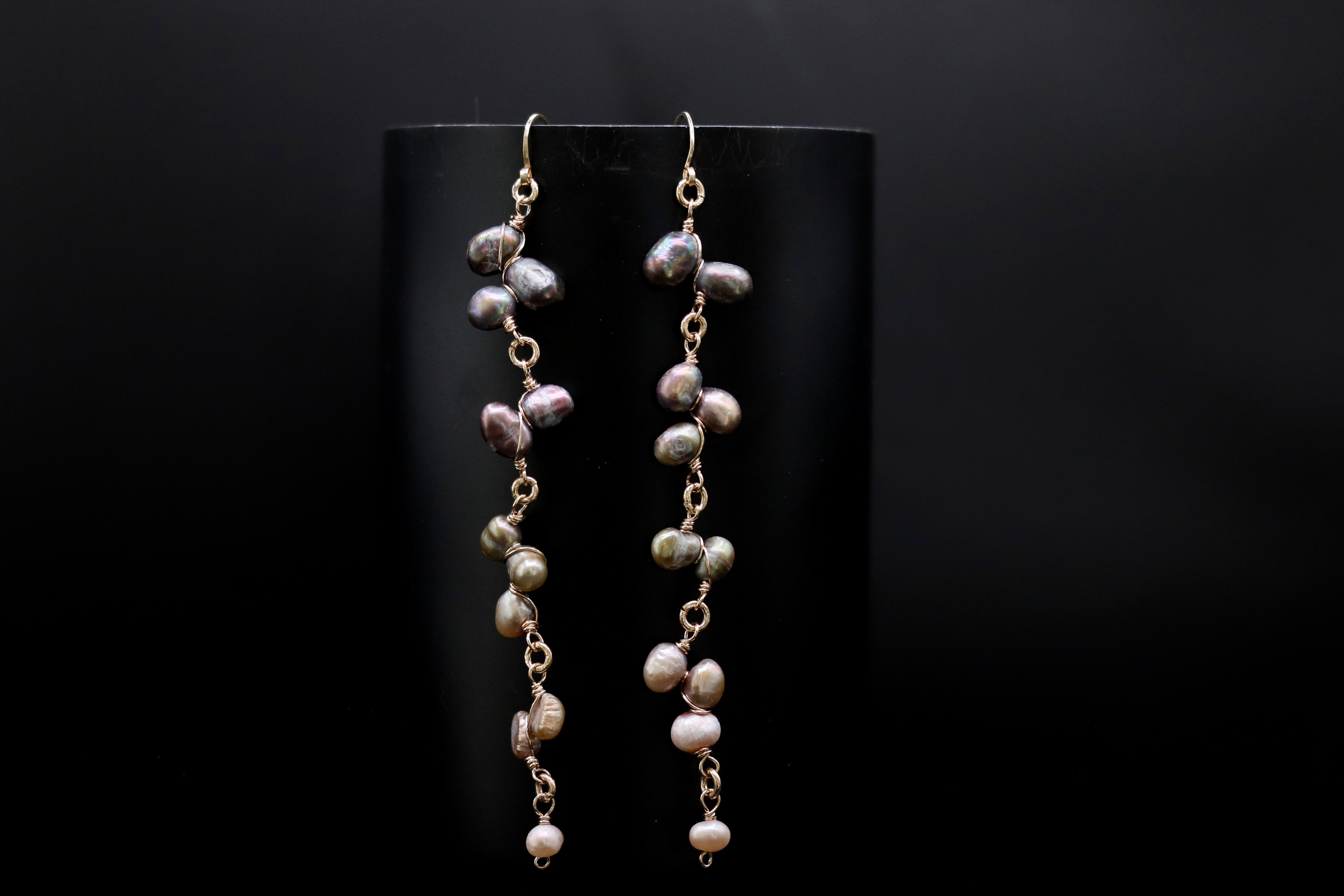 A pair of earrings with multiple strands of pearls hanging from a black background.