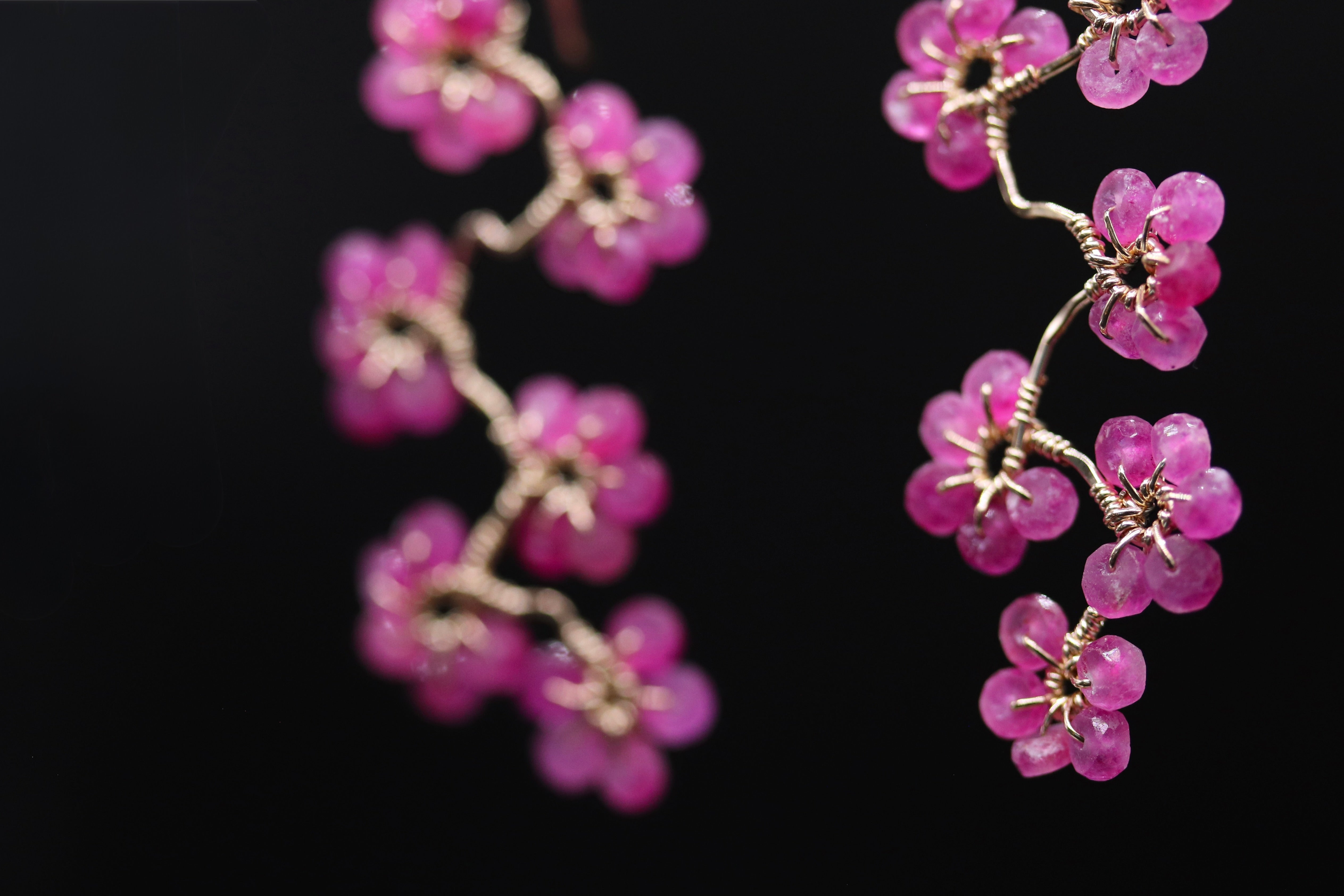 A close-up view of delicate pink flower-shaped earrings made of small, shiny beads against a dark background.