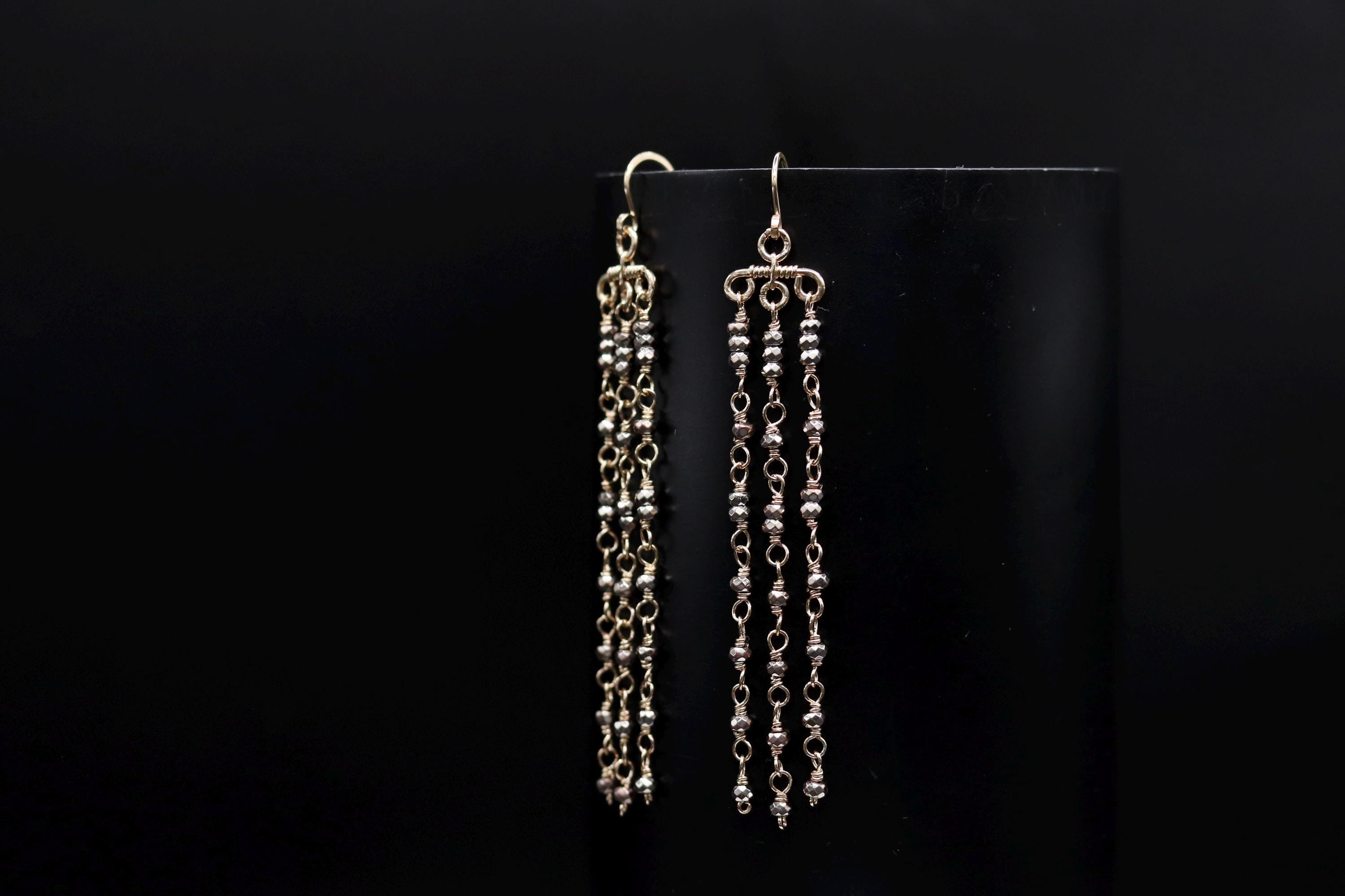 A pair of gold earrings with long, dangling chains and beads hanging from them, displayed against a black background.
