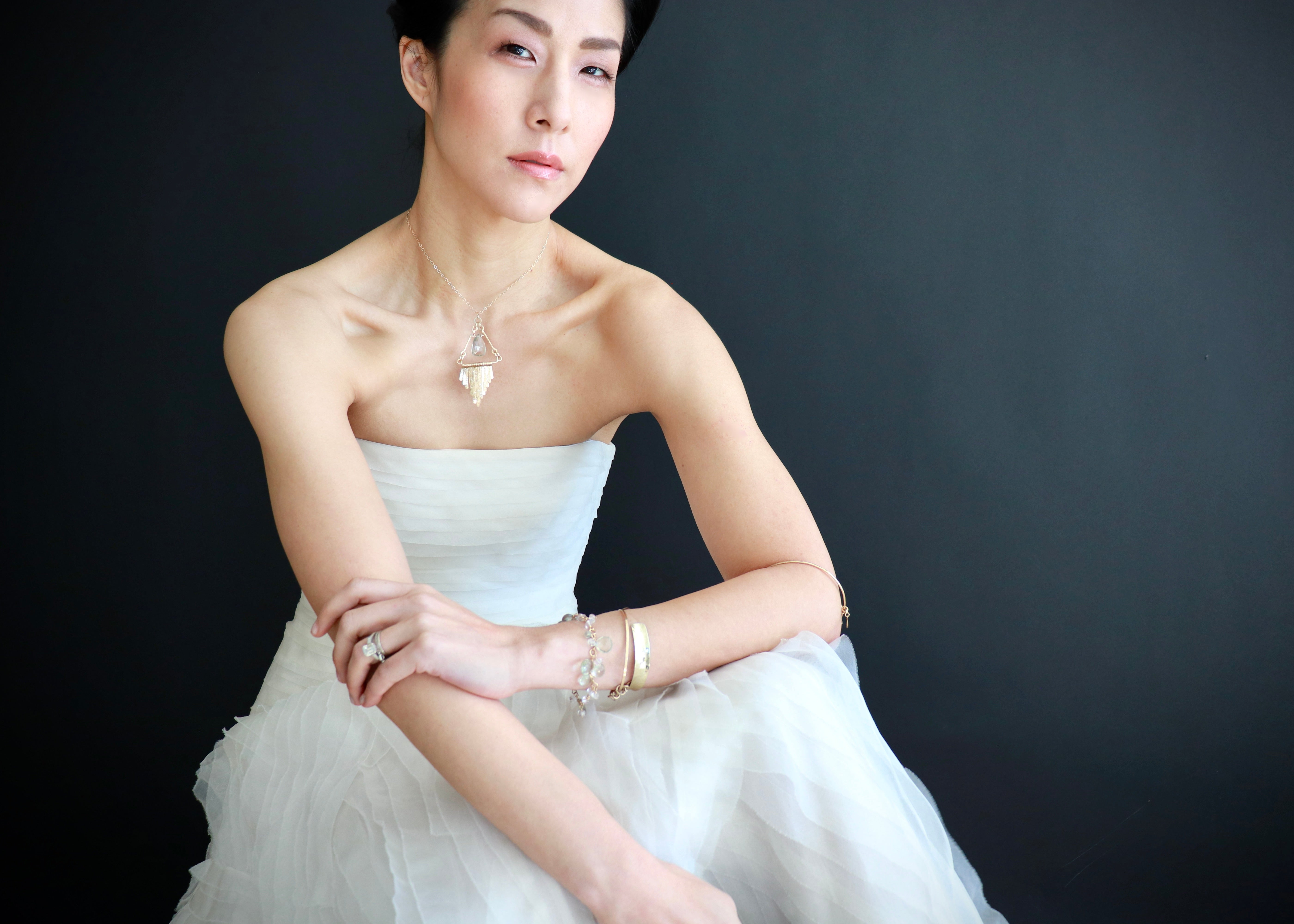 A woman in a white strapless dress poses against a dark background, her hands resting on her knees.