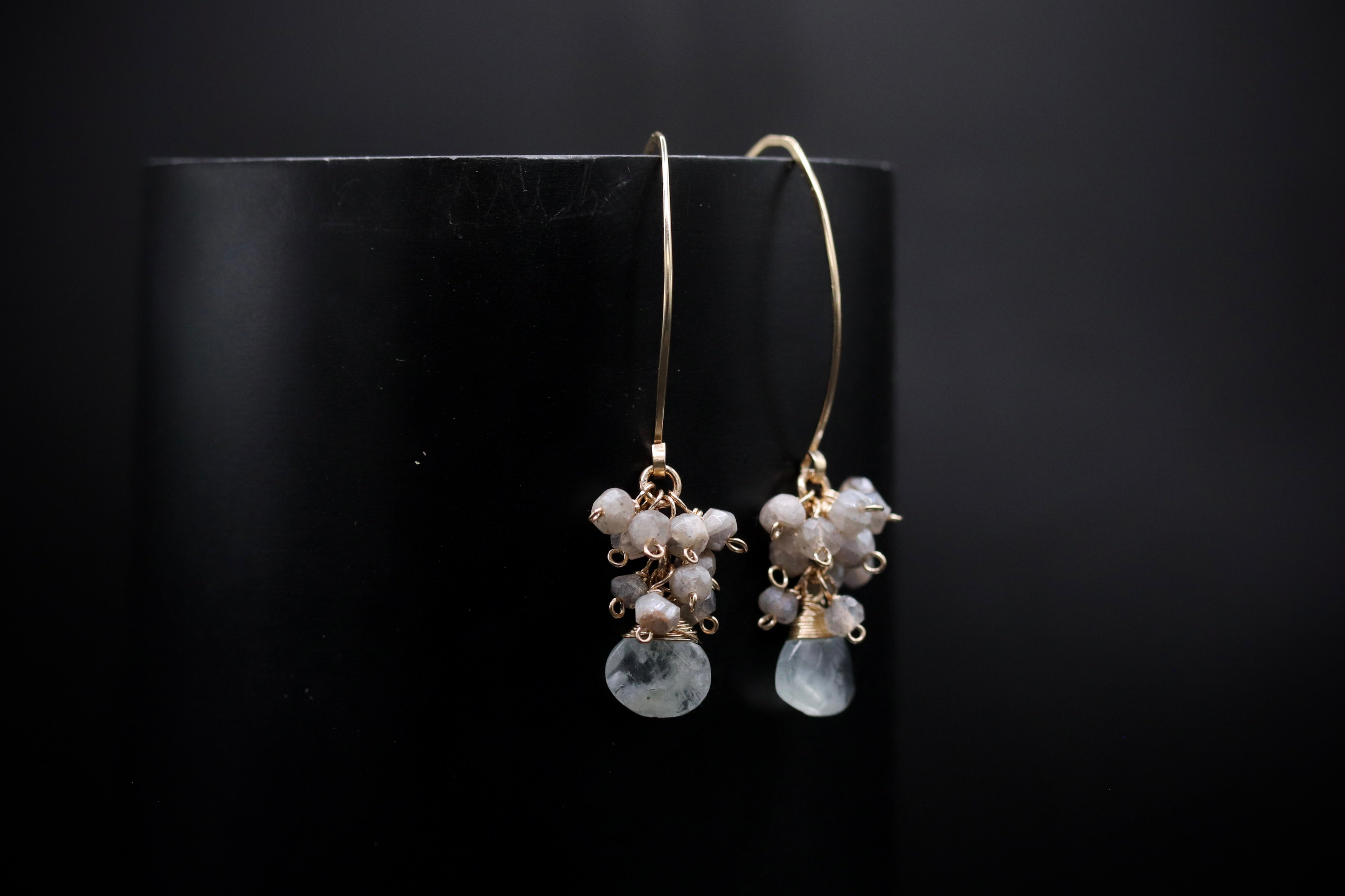 A pair of elegant earrings with white stones hanging from a gold hook against a black background.