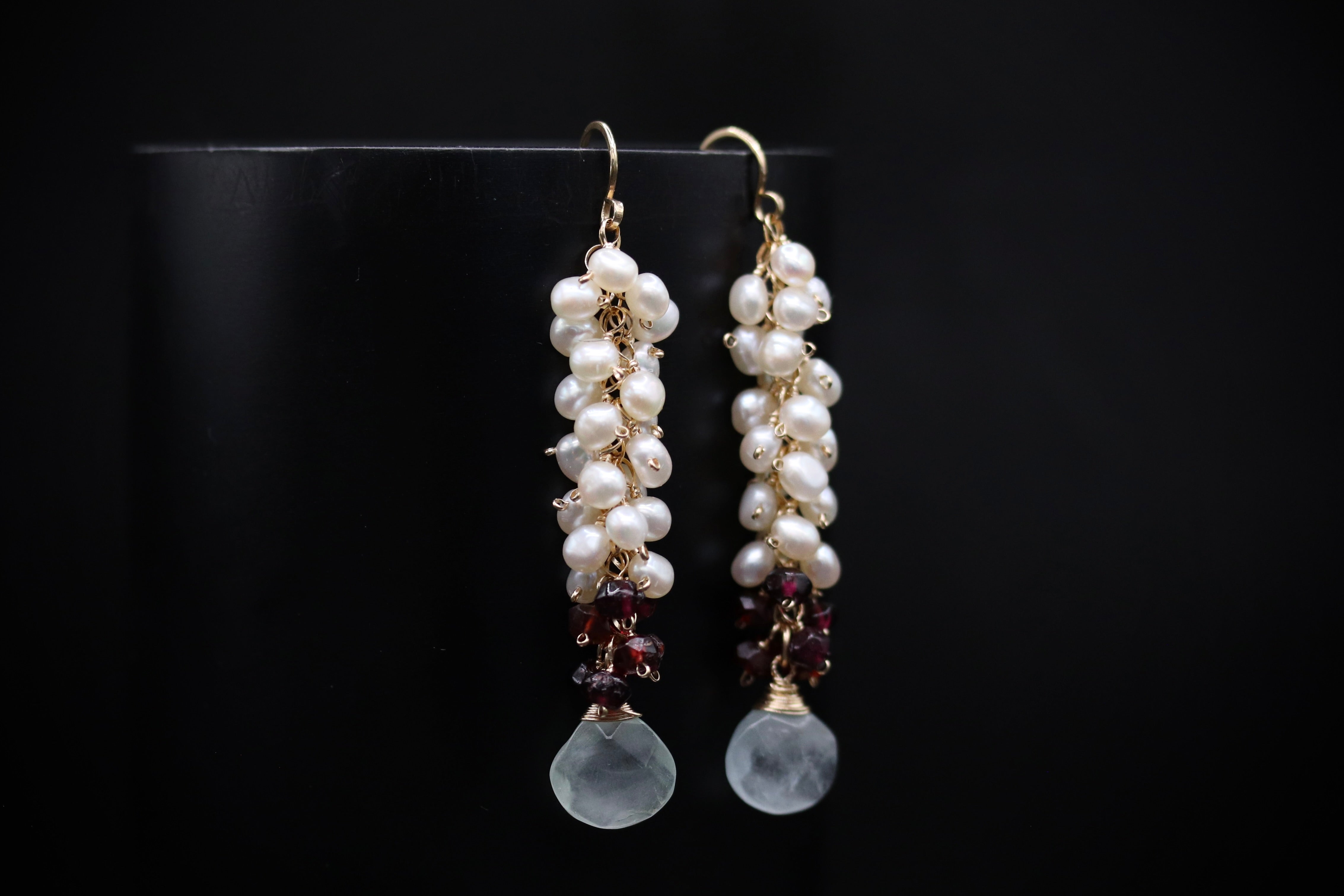 A pair of elegant earrings with white pearls and garnet stones hanging from the ends.