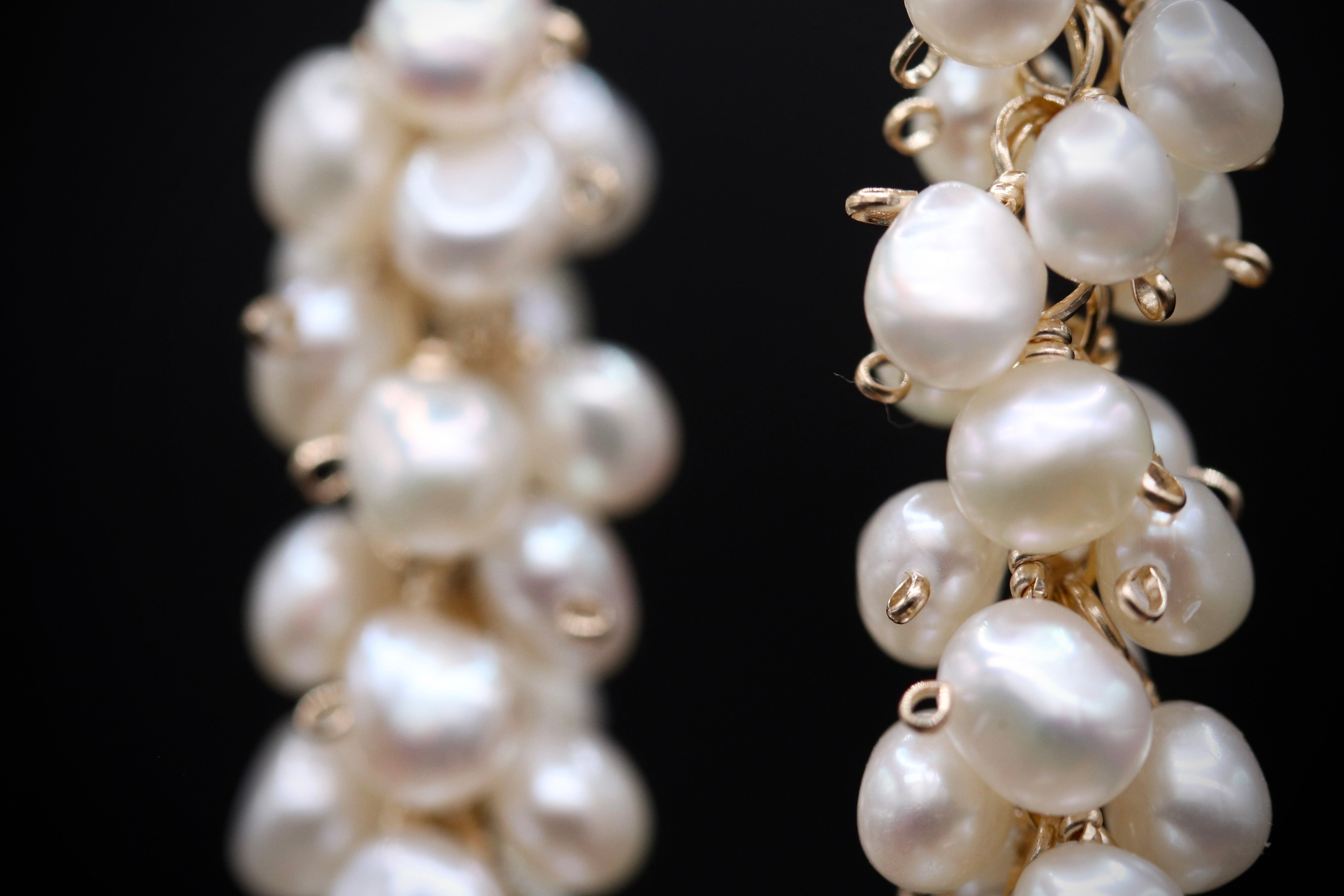 A close-up view of a pair of elegant earrings made of white pearls and gold-colored metal.