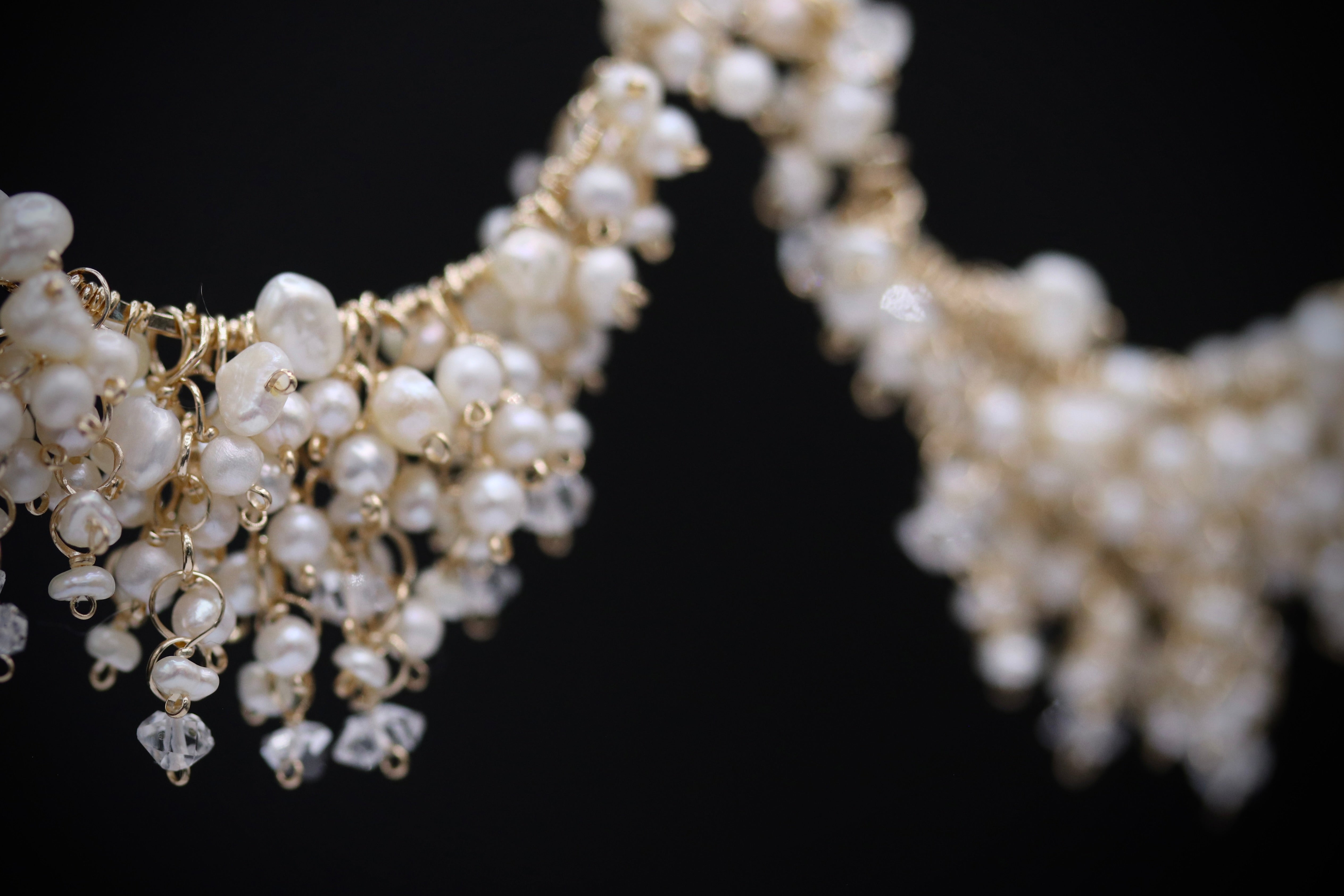 A close-up view of a delicate, ornate necklace with numerous small white pearls and clear gemstones, creating a sparkling and elegant design.